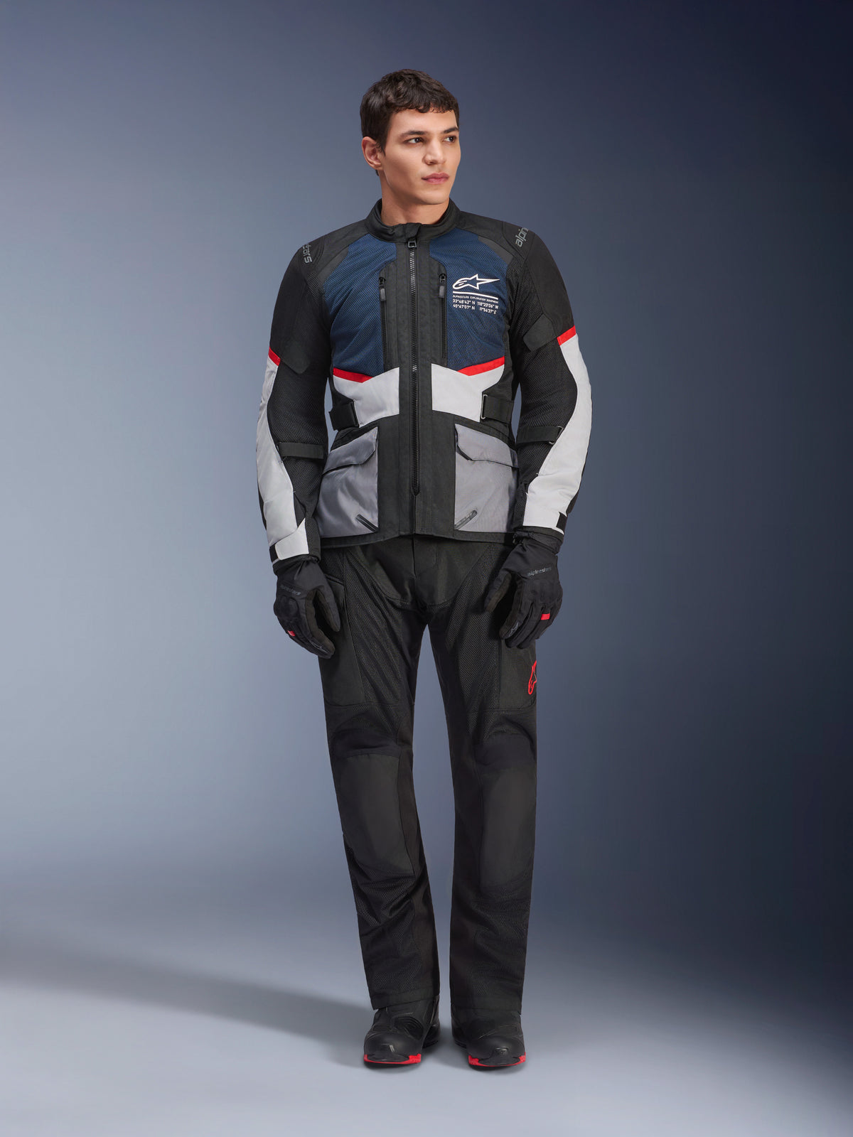 Chaqueta Alpinestars Andes Air Drystar®, chaqueta de moto touring, azul profundo, negro y gris hielo, combinada con pantalones y guantes de aventura negros a juego, con paneles de malla para ventilación y diseño técnico multibolsillos.