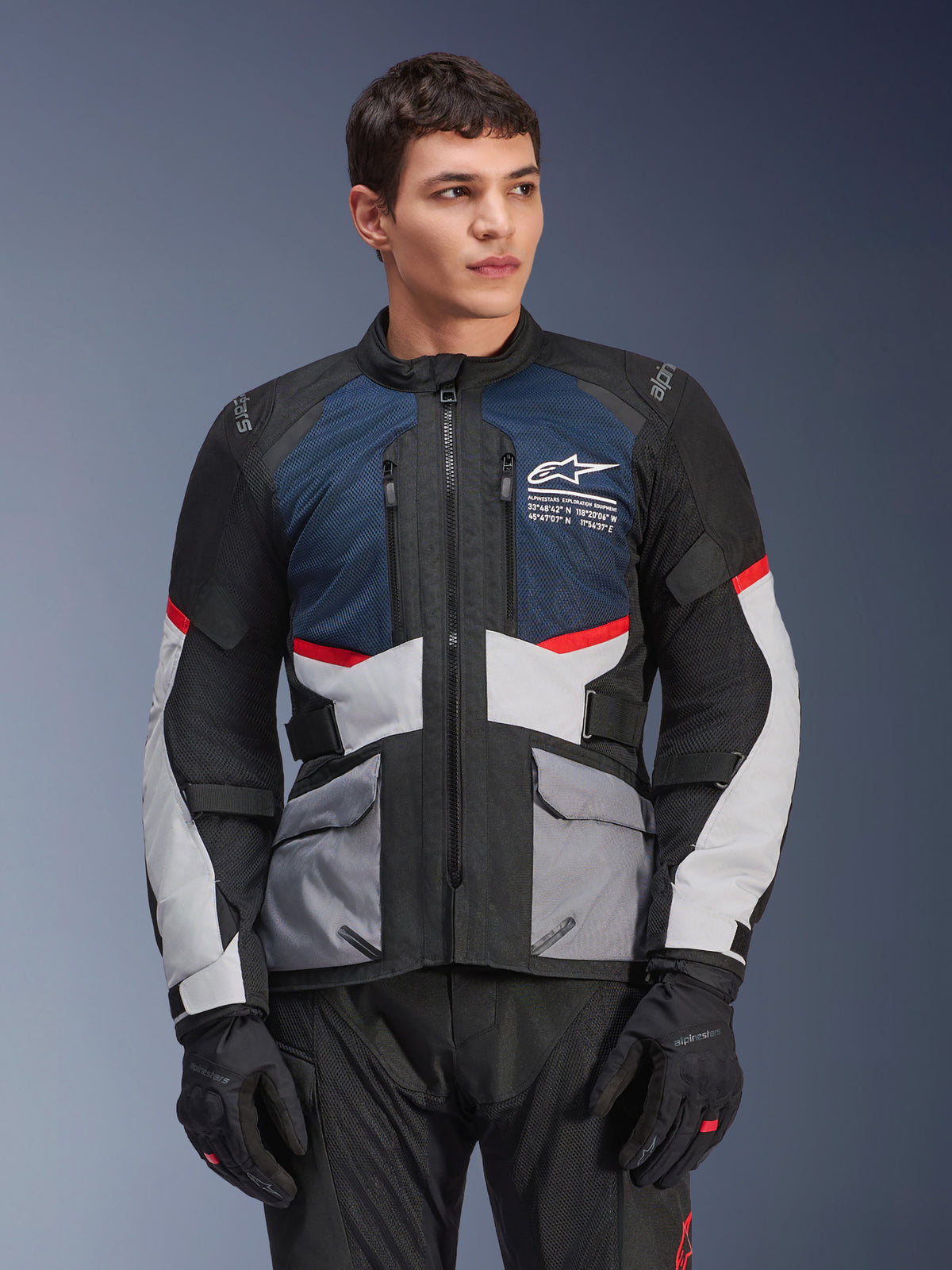 Alpinestars Andes Air Drystar® Jacket, chaqueta de moto touring, azul profundo, negro y gris hielo con detalles rojos, usada por un modelo masculino con guantes negros, con paneles de ventilación de malla y bolsillos frontales utilitarios, equipamiento moderno para aventura y conducción en carretera