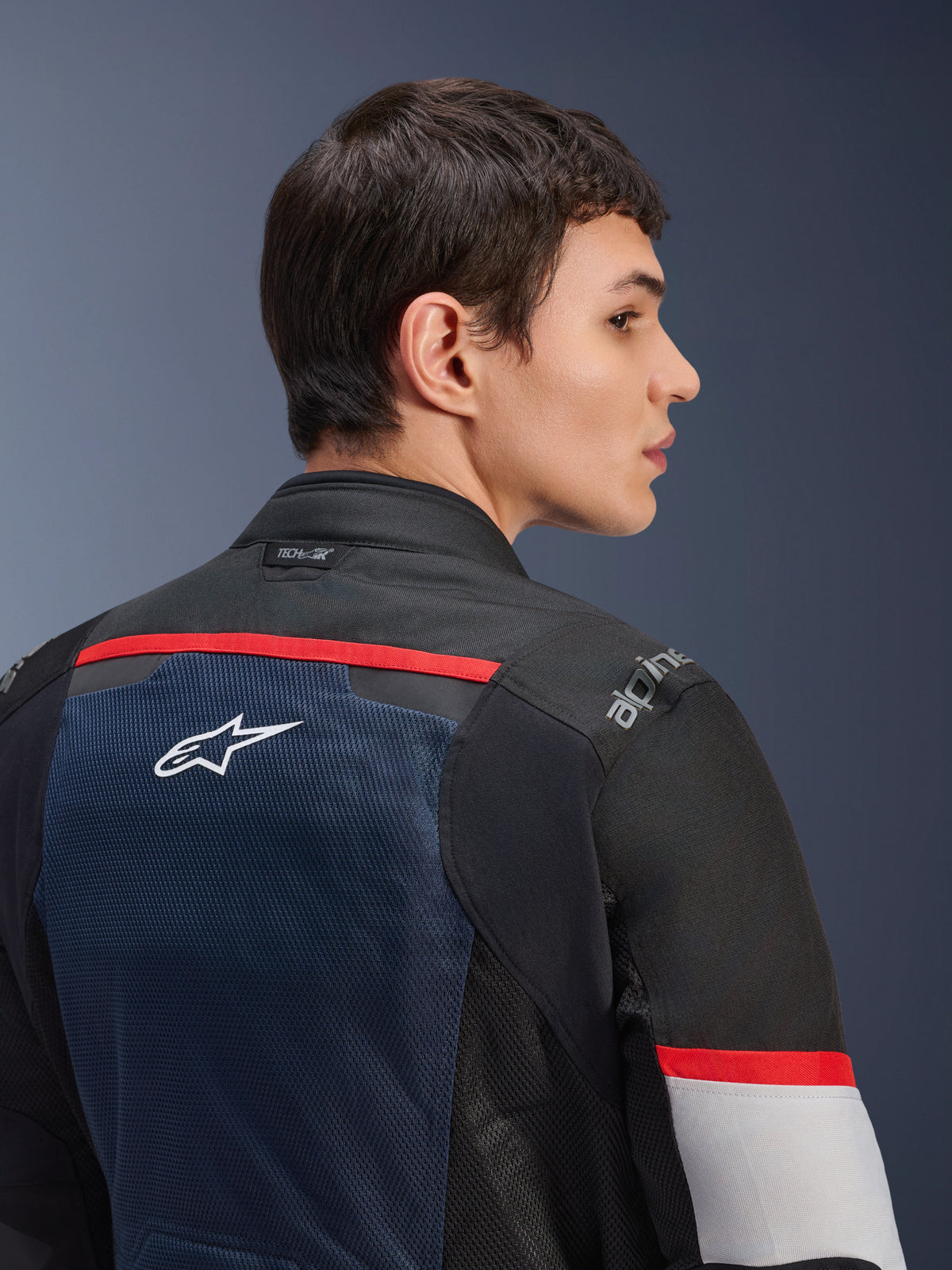 Chaqueta Alpinestars Andes Air Drystar®, azul profundo, negro y gris hielo, vista de cerca de la espalda en un modelo, con panel de malla transpirable con el logo de la estrella blanca, detalles en rojo y marca Tech-Air® en el cuello, equipamiento de moto de turismo para dos estaciones