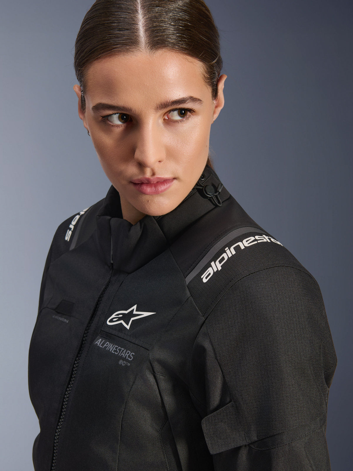 Chaqueta Alpinestars Stella Andes V4 Drystar® para mujer, chaqueta de moto negra, retrato de estudio en primer plano que muestra el torso superior y el hombro, con logotipos blancos de Alpinestars, material textil de alta calidad y un ajuste femenino elegante
