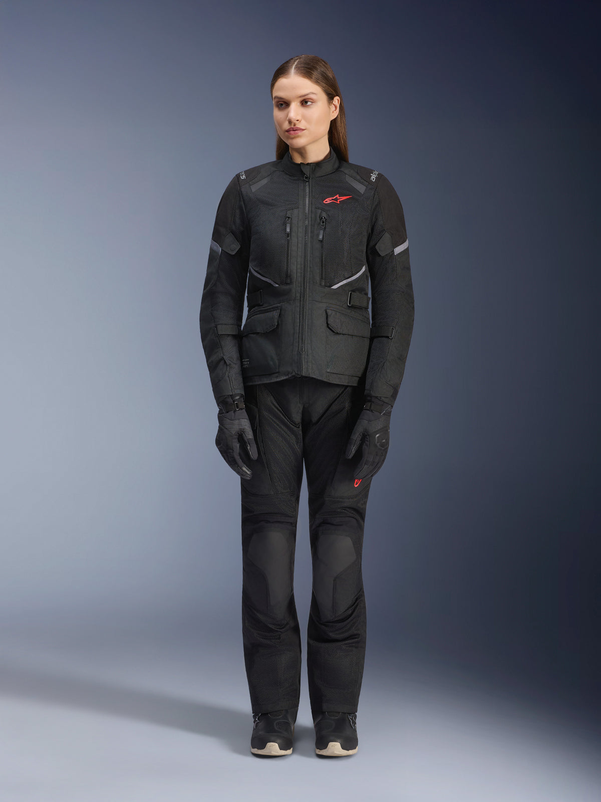 Female model wearing the Alpinestars Stella Andes Air Drystar® Jacket in Black, paired with matching black touring pants and gloves, featuring large mesh ventilation panels, red logo accents, and reflective details, professional studio shot for women's motorcycle gear.