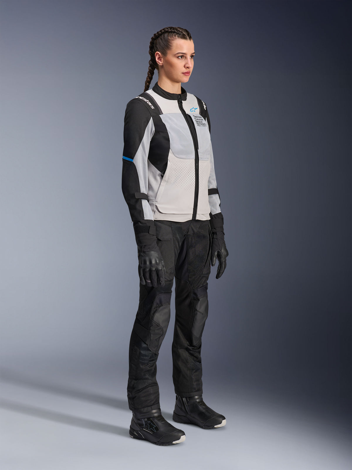 Model wearing the Alpinestars Stella ST-2 Air Jacket in Ice Gray and Black, women's technical motorcycle jacket with mesh panels and softshell construction, paired with black adventure touring pants and boots, featuring blue accents and a modern riding design
