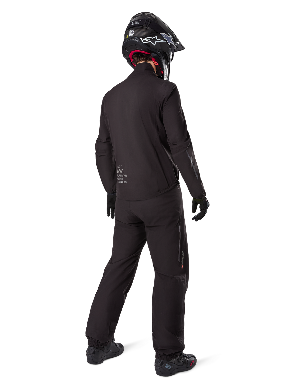 Motociclista visto desde atrás vistiendo los pantalones negros Amt-8 Stretch Drystar® XF y la chaqueta a juego, conjunto completo de adventure touring con casco y botas negras, equipamiento técnico impermeable y elástico para motociclismo de larga distancia