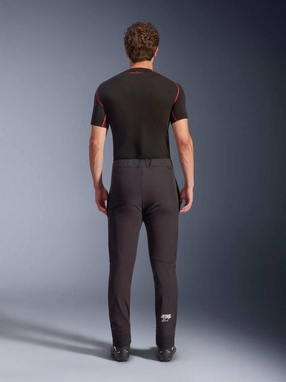 Alpinestars Aeroshell Pants, crossover sports softshell motorcycle pants, Black, rear view worn with a black short-sleeve base layer, featuring a slim fit, pre-curved knees, and white Astars logo on the lower left leg.