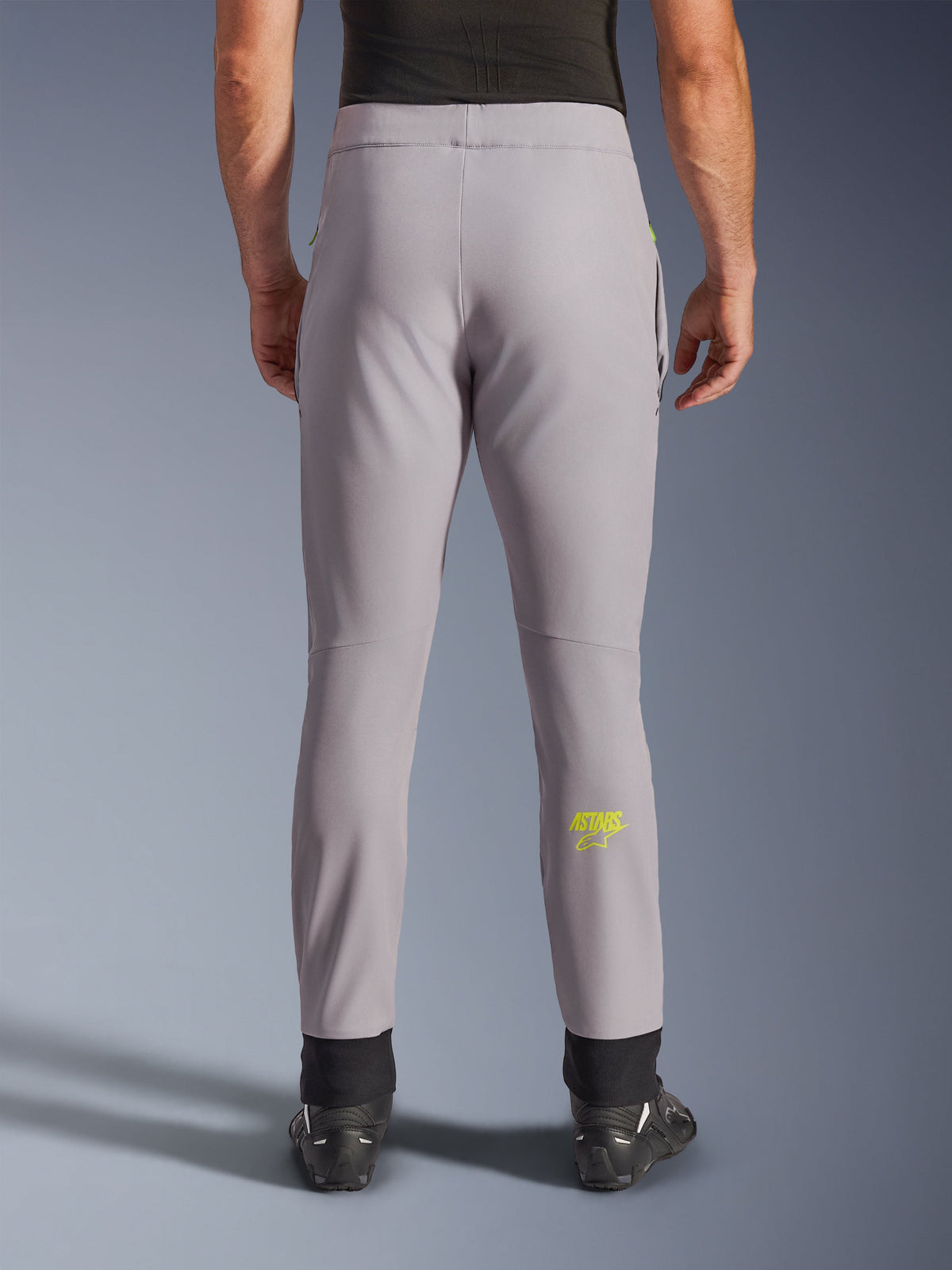 Pantalones Alpinestars Aeroshell, pantalones de moto, gris medio y amarillo flúor, vista trasera con el logo Astars amarillo en la pantorrilla, puños elásticos negros en los tobillos, diseño textil softshell moderno para uso en carretera y casual