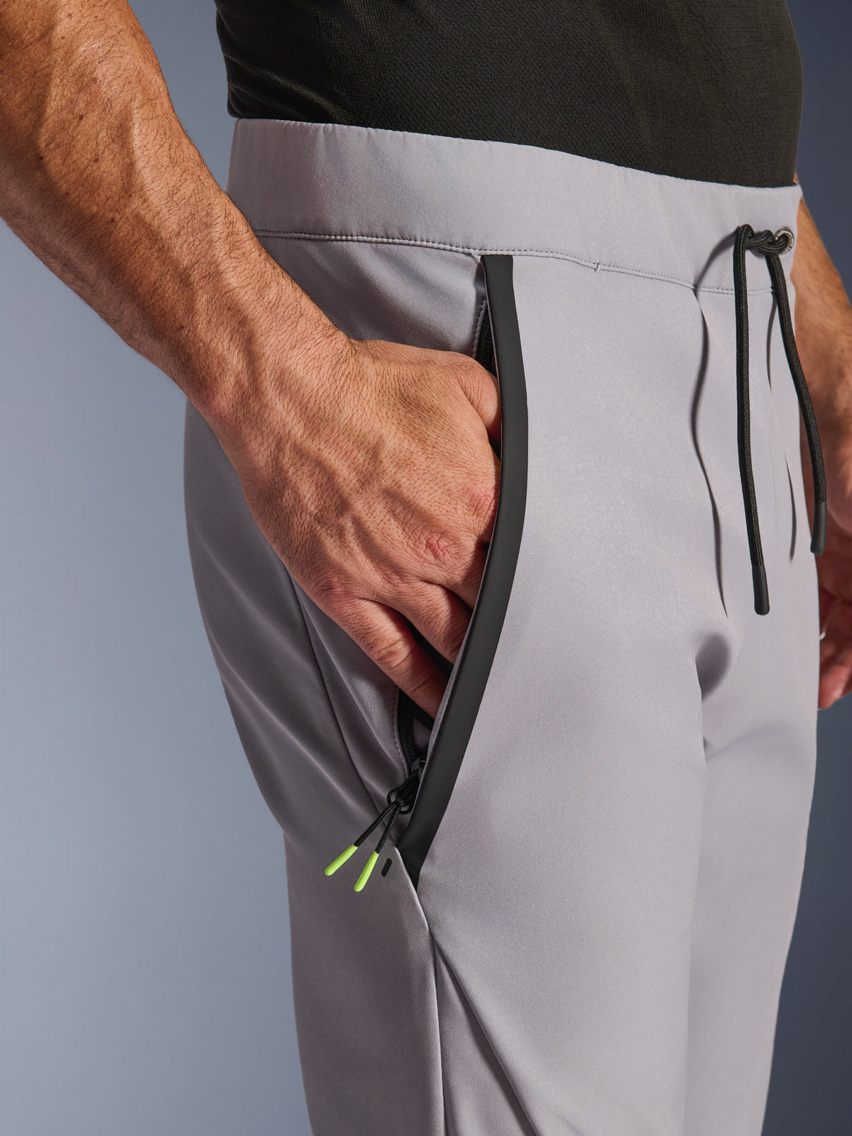 Pantalones Alpinestars Aeroshell, Gris Medio Amarillo Flúor, primer plano del bolsillo frontal con cremallera y la cintura, cremallera sellada negra con puntas en amarillo flúor, cintura elástica con cordón negro, pantalones de moto softshell deportivos crossover