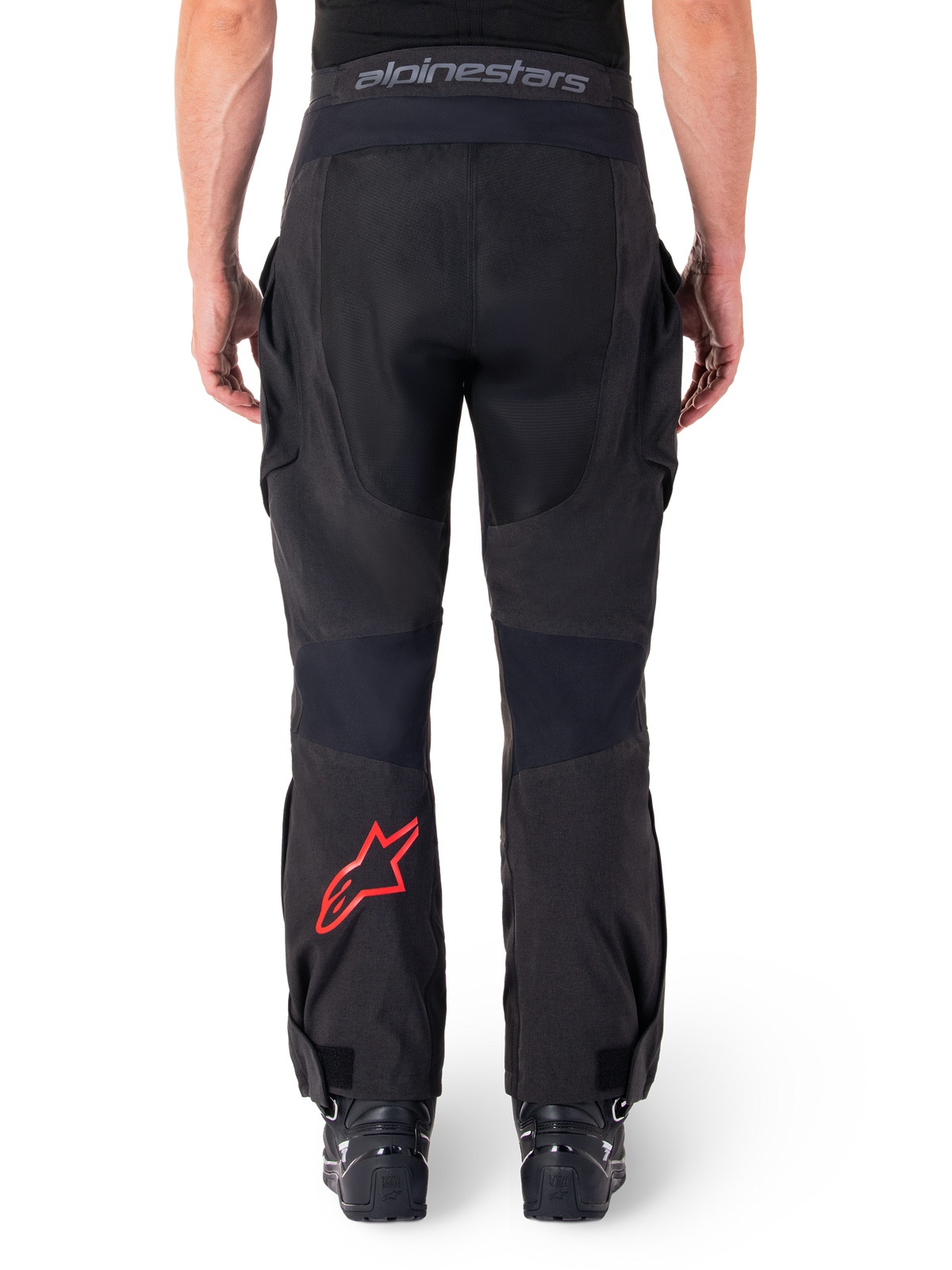 Pantalones Alpinestars Hyde XT Drystar®, pantalones de moto de aventura, negros con logotipo de estrella roja en la parte inferior de la pierna, vista trasera, diseño de enduro sobre la bota con paneles textiles resistentes y cinturilla con la marca.