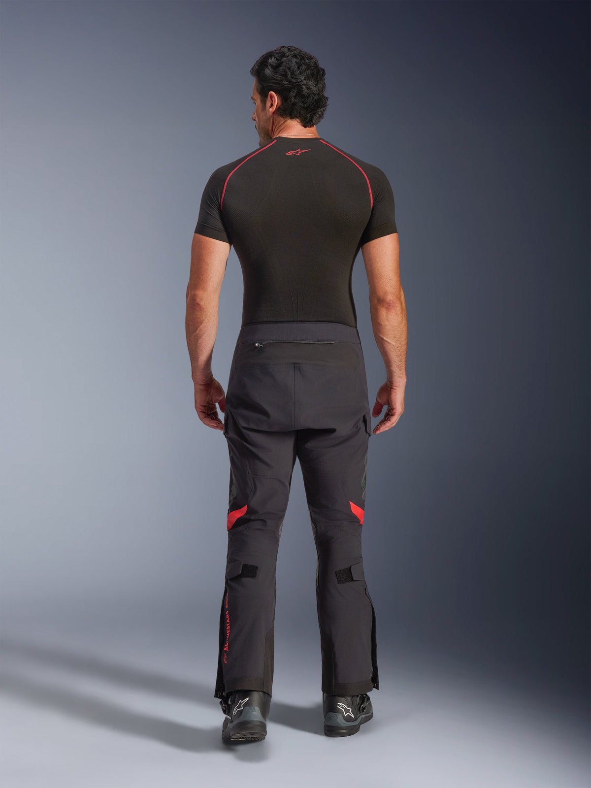 Alpinestars Halo Pro Drystar® XF Laminated Pants, Adventure Motorcycle Pants, Black Dark Shadow with red highlights, rear view worn with a black short-sleeve base layer and black adventure boots, showcasing a durable 3-layer laminated construction and ergonomic fit.