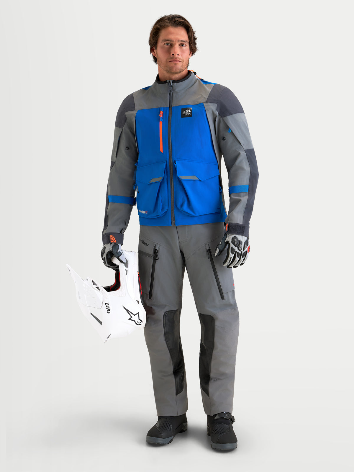 Alpinestars Maxdura Drystar XF Laminated Pantalones, pantalones de moto para aventura de hombre en gris oscuro y negro, membrana Drystar, vista frontal en modelo sosteniendo un casco todoterreno blanco