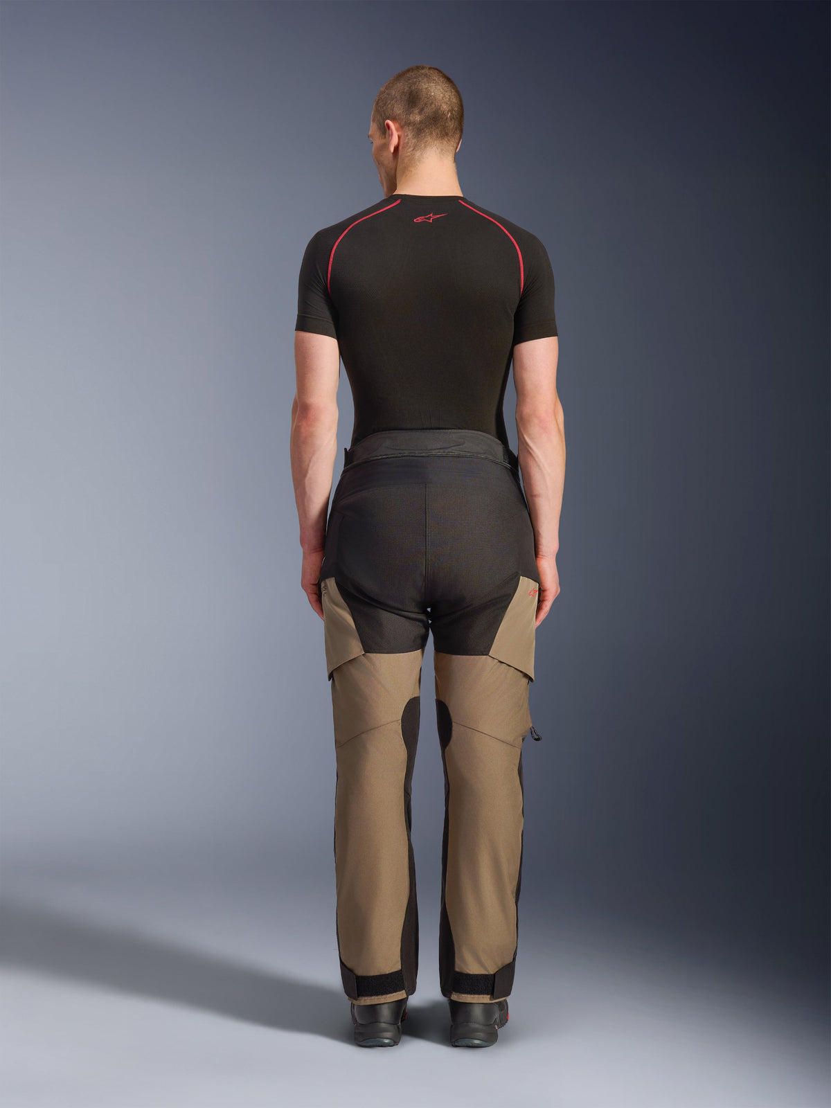 Pantalones Alpinestars Andes V4 Drystar®, pantalones de aventura para moto, color nogal y negro, vista trasera en un modelo, con paneles reforzados y construcción textil duradera para conducir en cualquier clima.