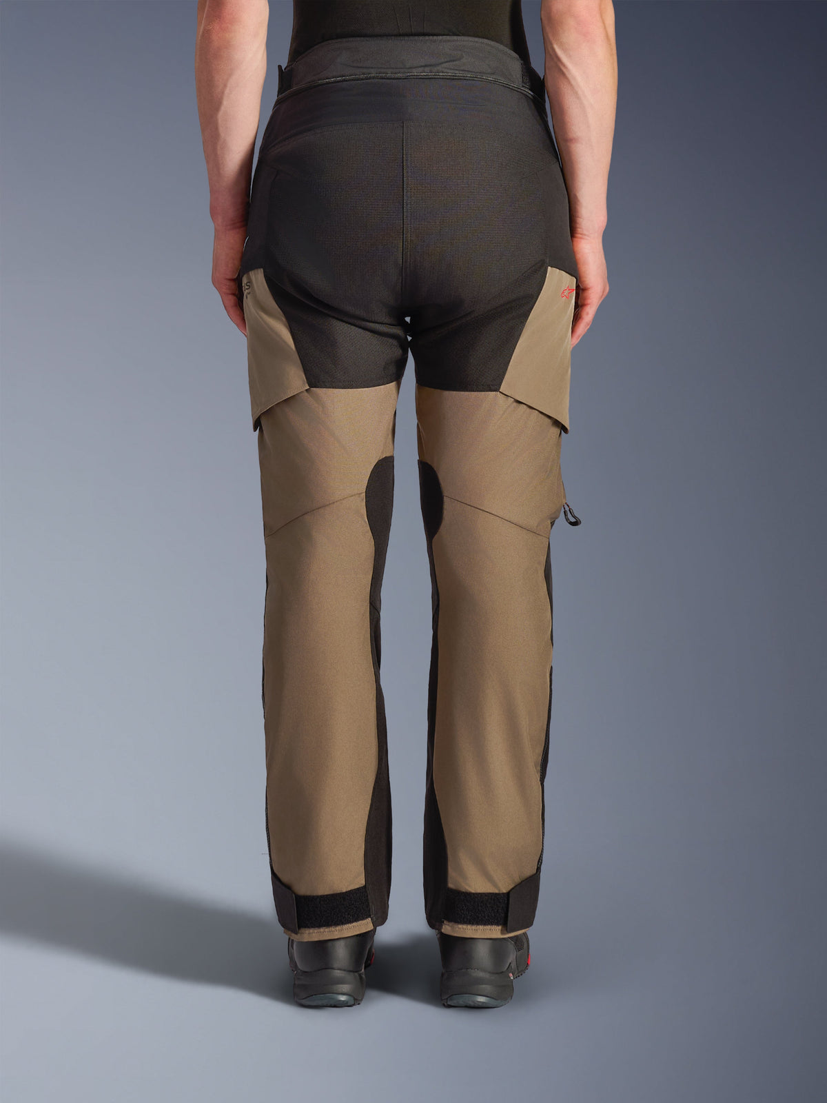 Alpinestars Andes V4 Drystar® Pants, pantalones de motociclismo Adventure Touring, color nogal y negro, vista trasera con paneles de asiento reforzados en negro, detalle de logotipo rojo y cierres de tobillo ajustables.