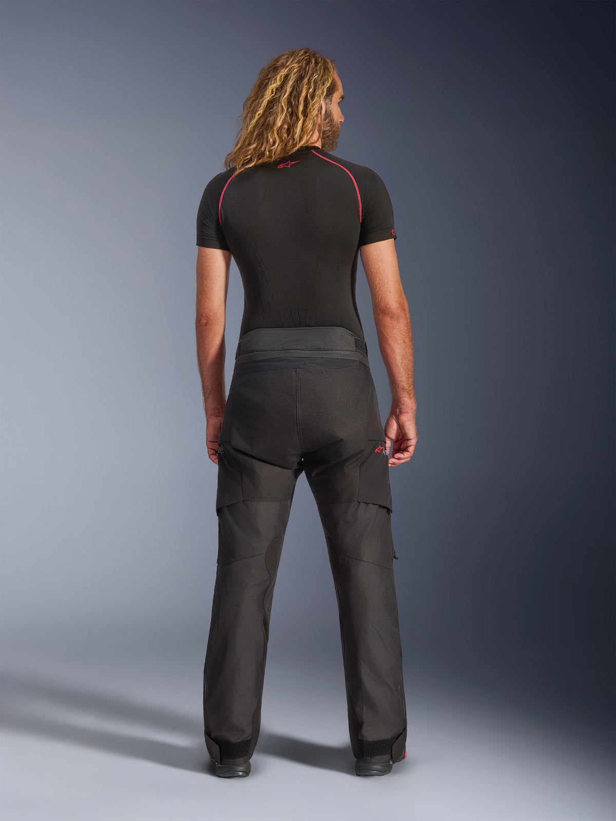 Pantalones Alpinestars Andes V4 Drystar®, pantalones de aventura para motociclismo, negros, vista trasera con una camiseta de compresión negra, con construcción textil reforzada y diseño técnico para turismo en todo tipo de clima.