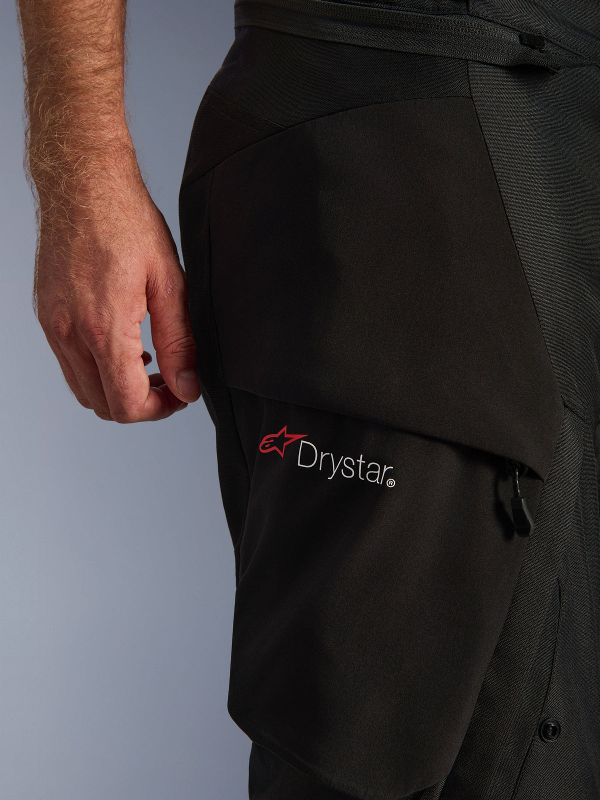 Pantalones Alpinestars Andes V4 Drystar®, primer plano de la zona del muslo, tejido textil negro, con el logotipo Drystar blanco y una estrella roja de Alpinestars, resaltando el material duradero y la construcción funcional de los bolsillos.