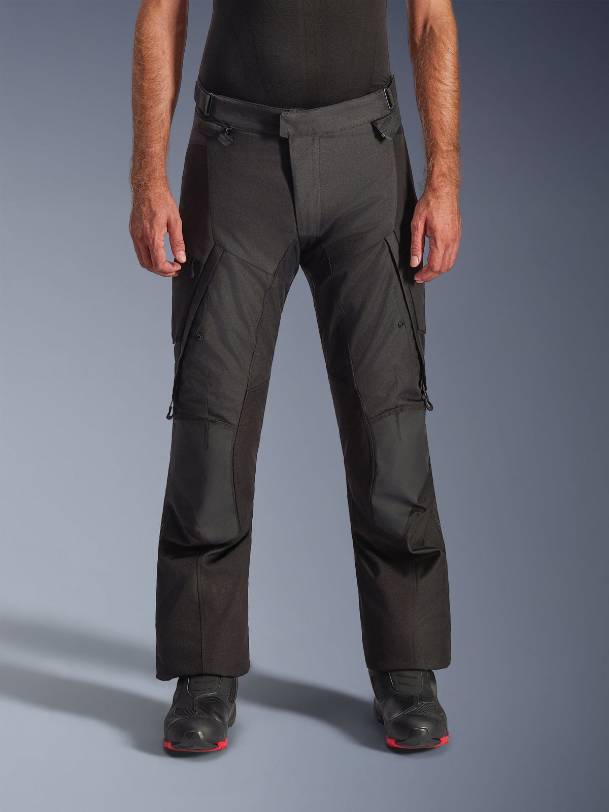 Alpinestars Andes V4 Drystar Pants, pantalones de moto para turismo de aventura, negros con paneles grises, con rodilleras reforzadas y bolsillos cargo en los muslos, usados con botas de moto negras, construcción textil impermeable para todo tipo de clima