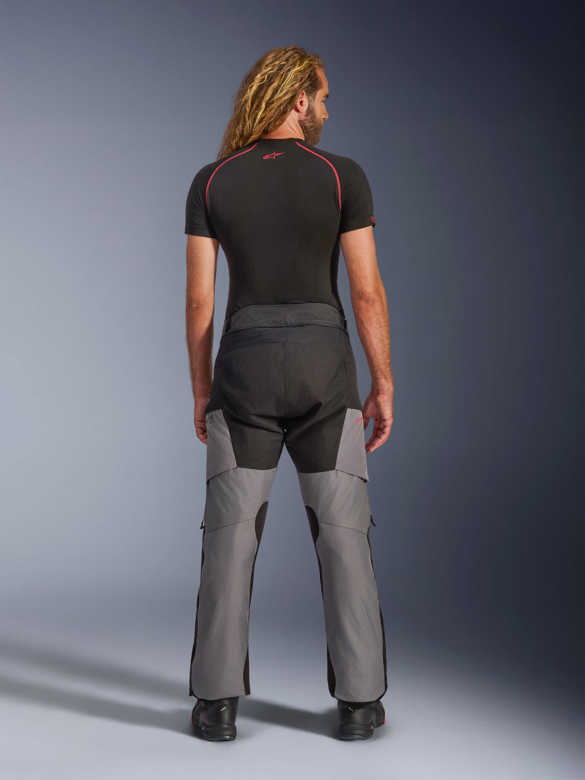 Pantalones Alpinestars Andes V4 Drystar®, pantalones de aventura para moto, negro y gris oscuro, vista trasera en un modelo, con paneles textiles reforzados en el asiento y las piernas, diseñados para turismo y desplazamientos en cualquier clima