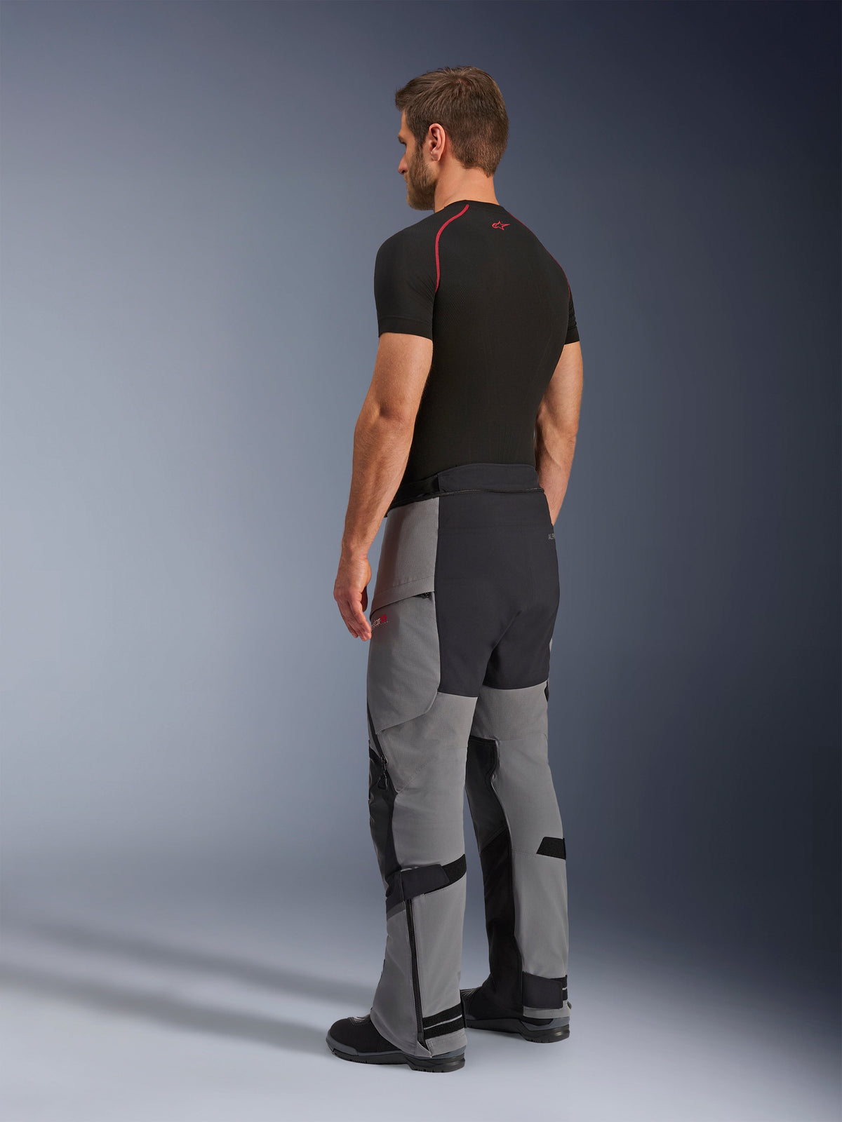 Alpinestars Andes Pro Drystar® XF Pants, Adventure Motorcycle Pants, Dark Gray and Black, rear three-quarter view on model, featuring technical textile construction with black reinforced panels on the seat and inner legs, worn with a black base layer t-shirt.