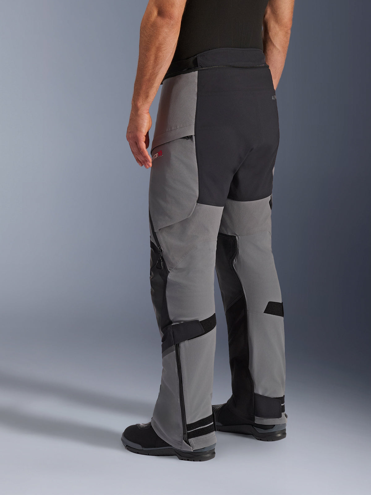 Pantalones Alpinestars Andes Pro Drystar® XF, pantalones de motociclismo de aventura, gris oscuro y negro, vista trasera de tres cuartos, con construcción textil con asiento y paneles internos de la pierna reforzados en negro, cremalleras en la parte inferior de la pierna y correas ajustables.