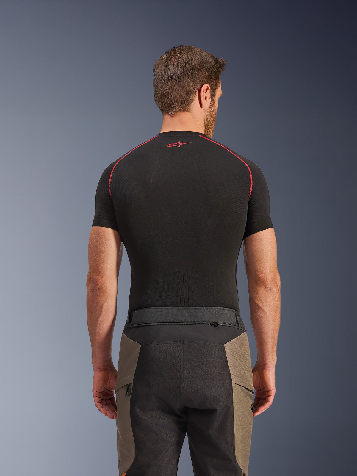 Pantalones Alpinestars Cusco Drystar®, pantalones de adventure riding, Walnut Black, vista trasera que muestra detalles de la cintura y diseño de bloques de color, usados con una capa base negra de manga corta con costuras rojas y logotipo
