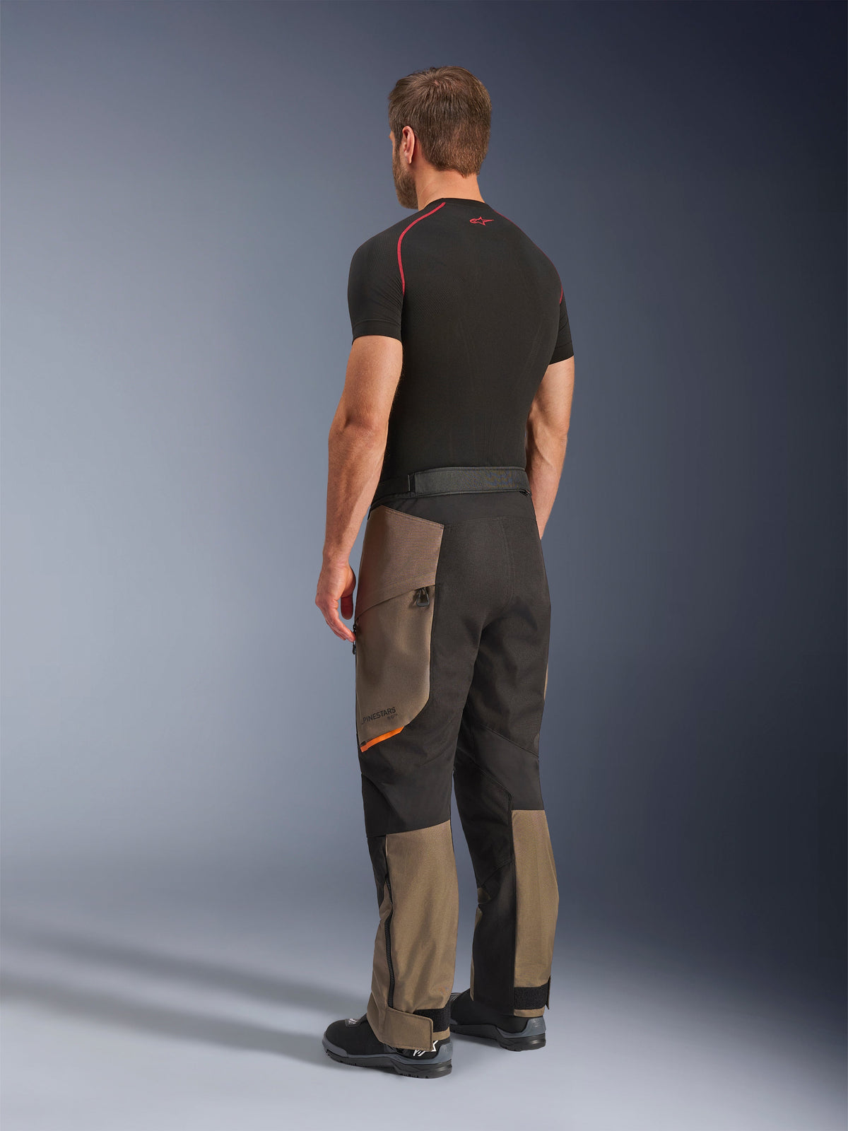 Alpinestars Cusco Drystar® Pants, pantalones de motociclismo adventure, Walnut Black, vista trasera de tres cuartos usados con una capa base negra y botas, con paneles textiles reforzados, bolsillos de carga con cremallera en los muslos y un ajuste touring ergonómico.