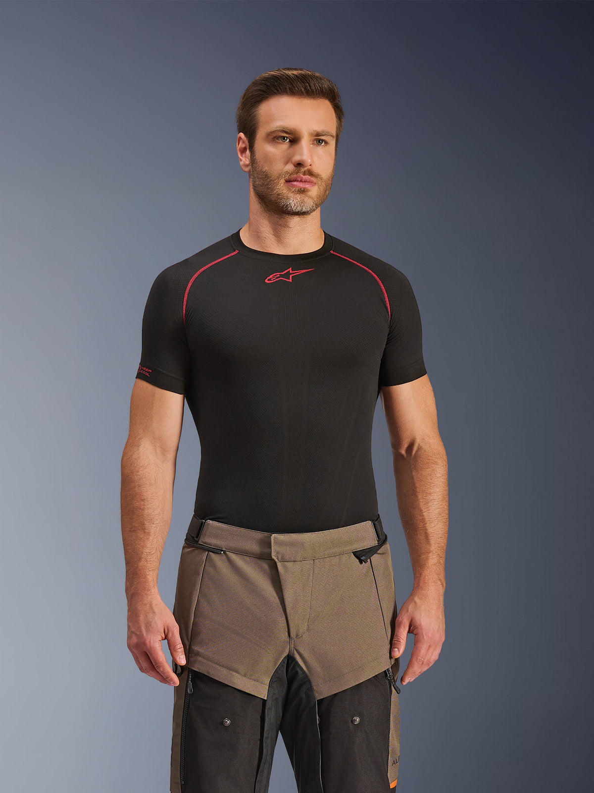 Pantalones Alpinestars Cusco Drystar®, pantalones de motociclismo adventure en color Walnut Black, usados por un modelo con una camiseta técnica de capa base Alpinestars negra, con un diseño textil bitono en marrón y negro con paneles reforzados para touring.