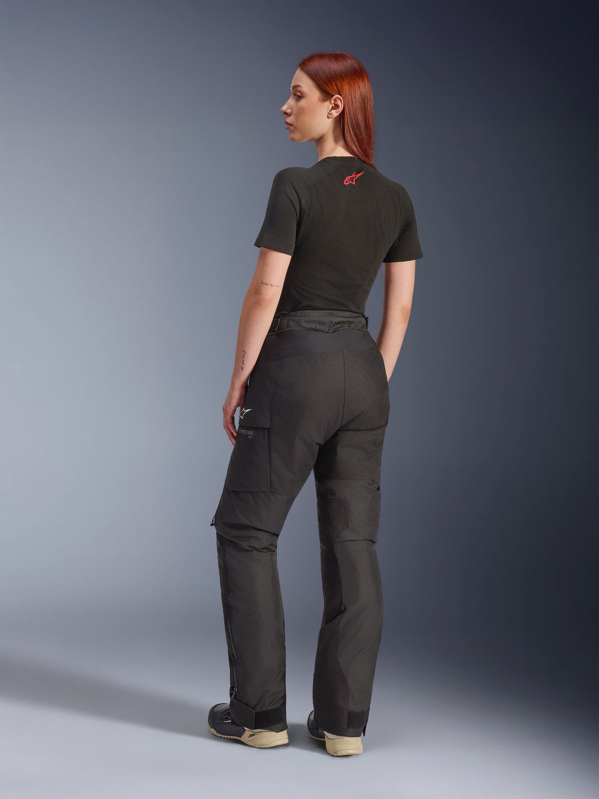 Alpinestars Stella Andes V4 Drystar® Pants, Black, adventure motorcycle pants shown from a rear side angle on a model, paired with a black t-shirt and boots, featuring side cargo pockets with white logo branding and durable textile construction.