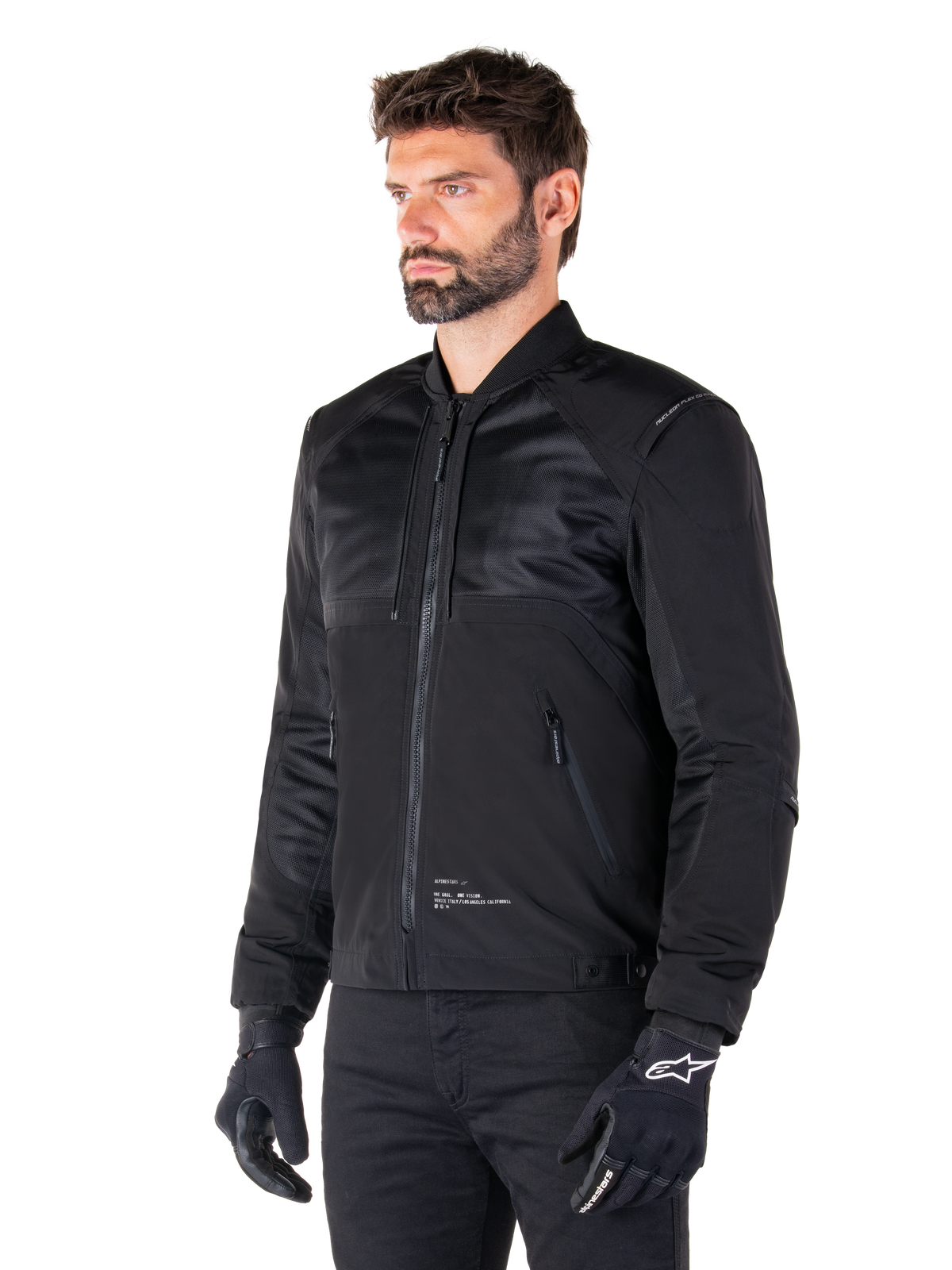 Parka impermeable Alpinestars Mootant, chaqueta de moto modular negra mostrada en su configuración bomber con paneles de malla en la parte superior del cuerpo y cuello acanalado, usada por un modelo con guantes y pantalones de conducción negros, estilo streetwear urbano contemporáneo.