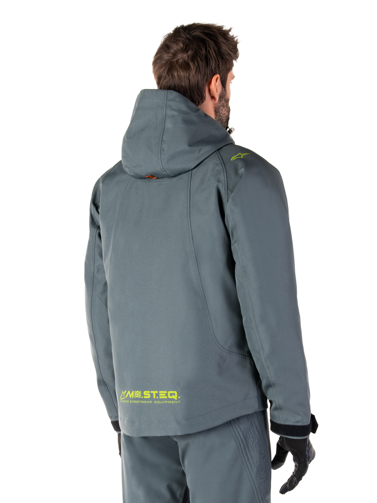 Alpinestars Morush Waterproof Parka in Urban Gray, rear view, featuring yellow MO.ST.EQ. branding on the lower back and shoulder, minimalist hooded design, worn with matching gray riding pants and black gloves, urban motorcycle streetwear.