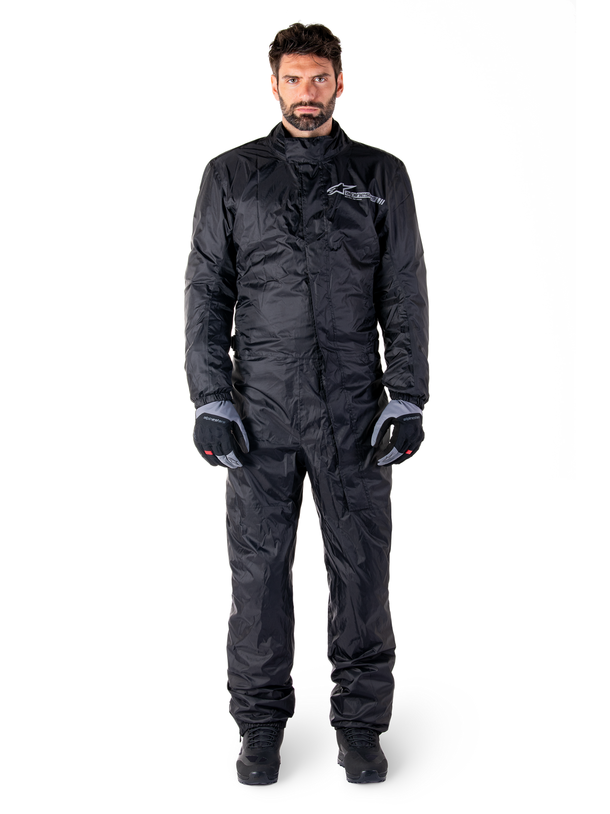 Alpinestars Hurricane Rain V2 Suit, traje impermeable de cuerpo completo para moto en negro, equipo de protección impermeable con cuello alto y cierre frontal contra tormentas, con logotipo blanco en el pecho, usado con guantes y botas en negro y gris