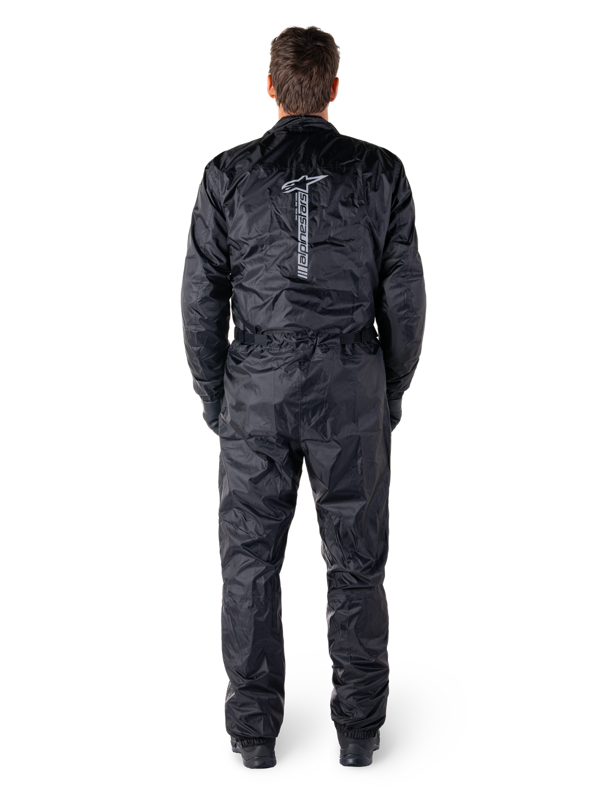 Mono Hurricane Rain V2 de Alpinestars, traje de moto impermeable de una pieza en color negro, vista trasera que muestra el logotipo y la marca denominativa vertical de Alpinestars en grande, tejido ligero arrugado con cintura y puños elásticos, diseñado para la protección al conducir bajo la lluvia.