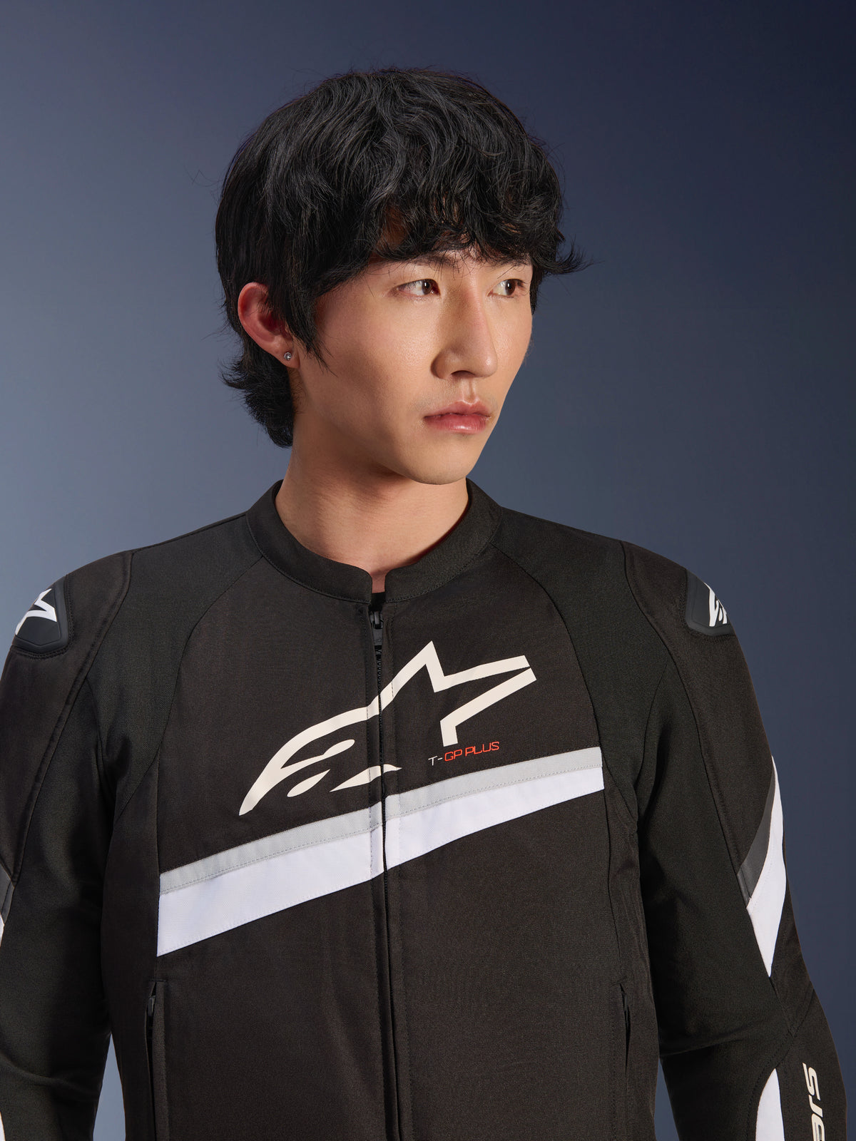 Alpinestars Chaqueta T-GP Plus R V4, negro y blanco, chaqueta textil de moto usada por un modelo masculino, con un gran logotipo de estrella blanca en el pecho, franjas diagonales blancas y protectores de hombros DFS Lite, equipo de conducción urbana de inspiración deportiva.