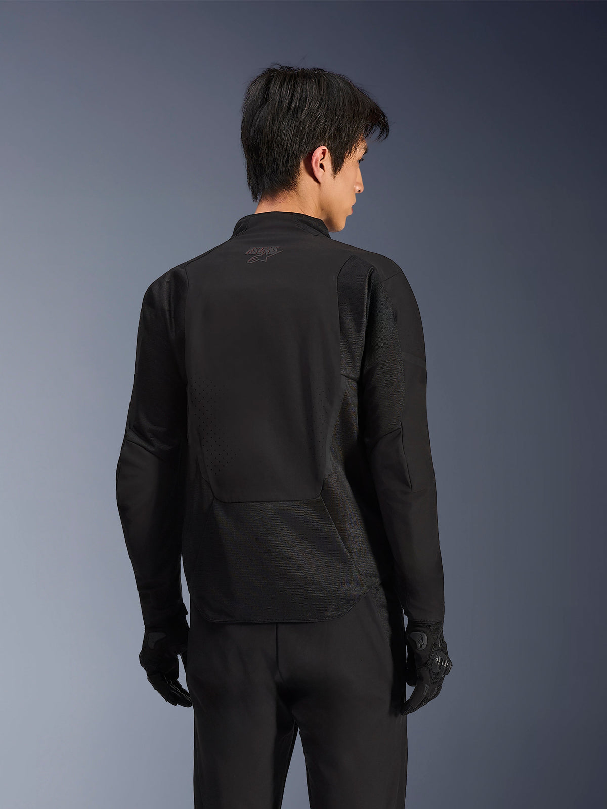Alpinestars Aeroshell Airflow Jacket, Black Anthracite, back view of sport motorcycle jacket featuring laser-perforated ventilation zones and 2D mesh panels, elongated rear for coverage, worn with black riding gloves