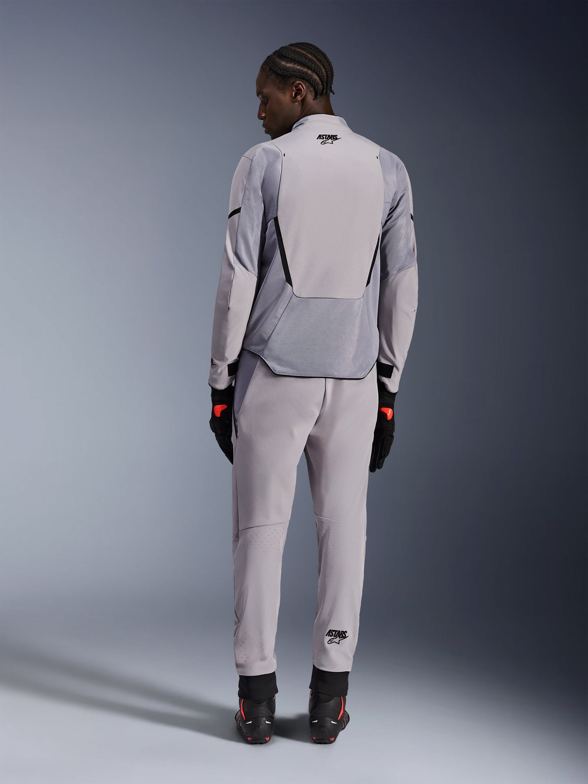 Chaqueta Alpinestars Aeroshell Airflow, Mid Gray Anthracite, vista trasera en un modelo, con paneles de malla técnica y zonas de ventilación perforadas con láser, combinada con pantalones grises a juego y equipamiento de moto negro, diseño de corte deportivo para alto rendimiento.