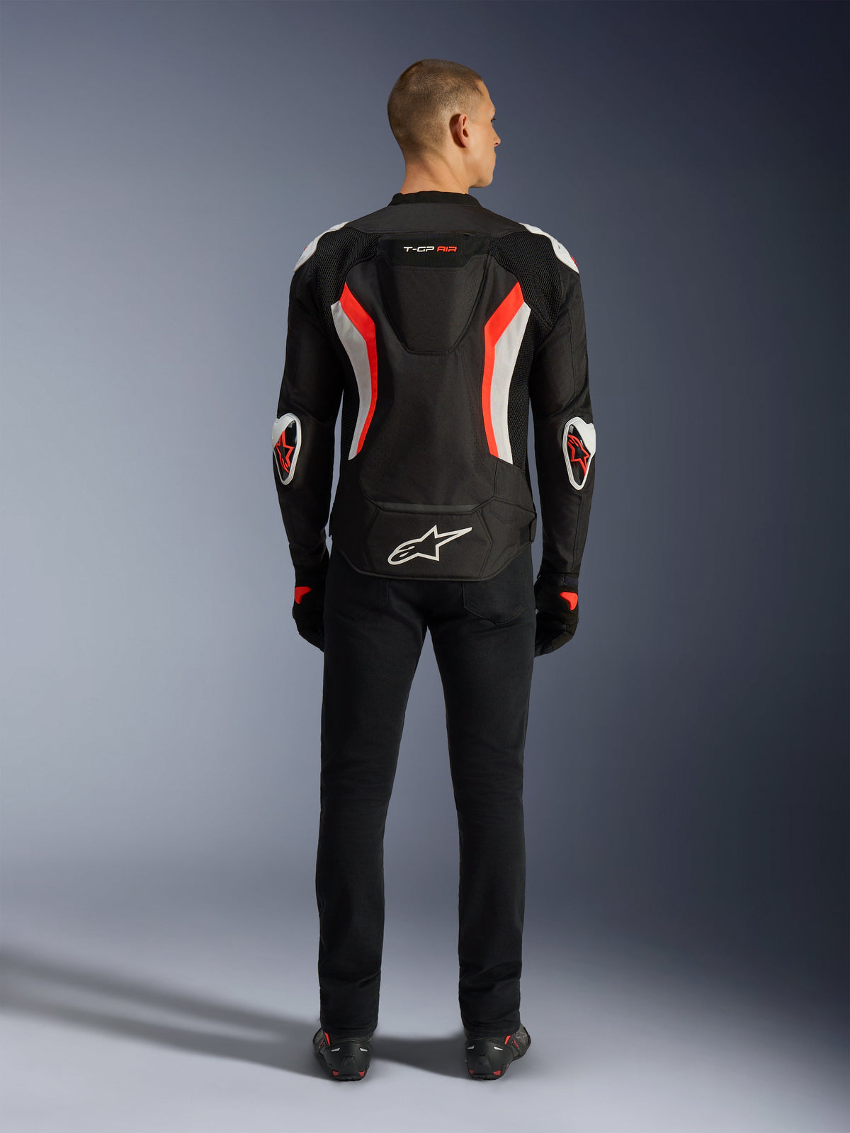 Chaqueta Alpinestars T-GP Air, chaqueta de moto, negro y rojo flúor, vista trasera en un modelo, con joroba aerodinámica, detalles en blanco y rojo fluorescente, logotipo de Alpinestars en la parte baja de la espalda, diseño de corte deportivo para conducción en carretera