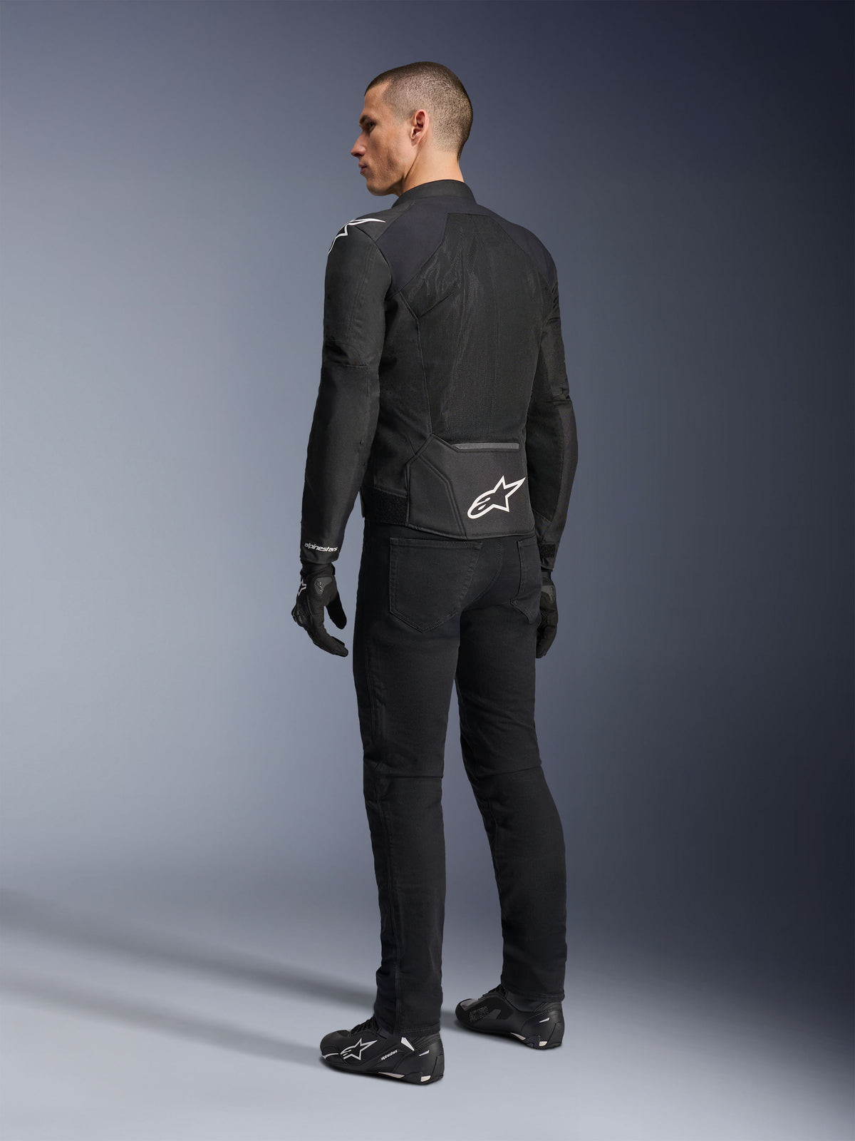 Alpinestars Viper Air V4 Jacket, Black textile motorcycle jacket, rear view on a male model, featuring large tech mesh panels for airflow and a white star logo on the lower back, worn with matching black riding pants and gloves