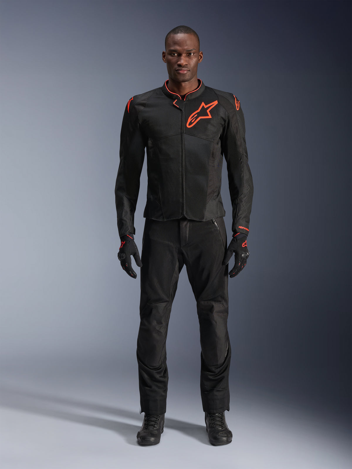 Alpinestars Viper Air V4 Jacket in Black Red Fluo, worn by a model with matching black pants and gloves, featuring mesh panels for airflow and a prominent red Alpinestars logo on the chest, sporty motorcycle road gear.