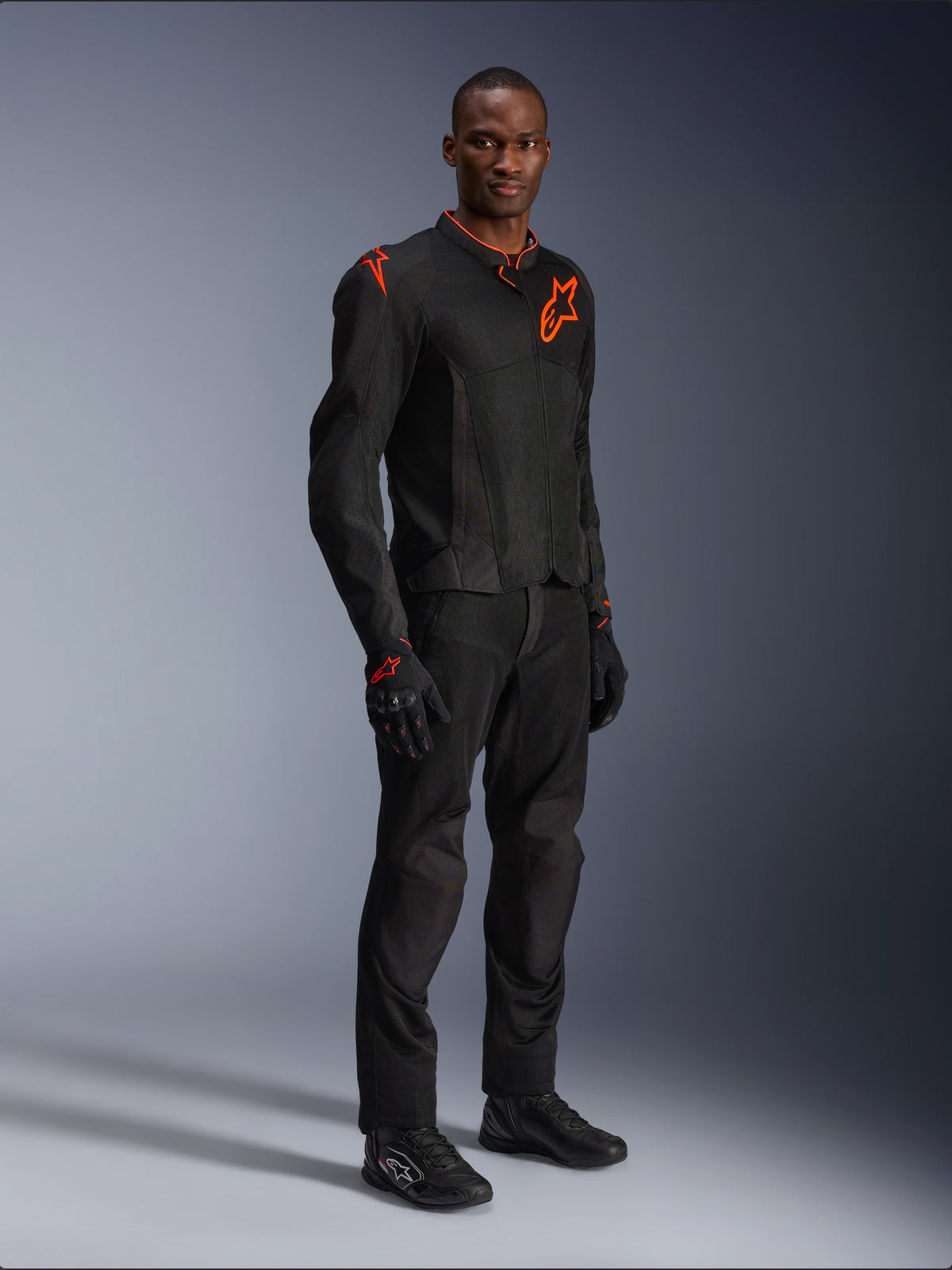 Model wearing Alpinestars Viper Air V4 Jacket in Black and Red Fluo, featuring mesh panels and red star logos on the chest and shoulder, paired with matching black motorcycle pants, gloves, and riding shoes, professional road riding gear ensemble