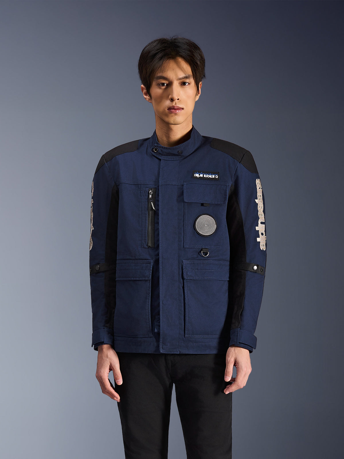 Chaqueta Alpinestars Dice, chaqueta de moto urbana, azul oscuro y negro, con diseño de chaqueta de campo multibolsillos, parche de espiral en el pecho y marca Alpinestars blanca en las mangas, prenda de conducción moderna inspirada en la ropa de trabajo