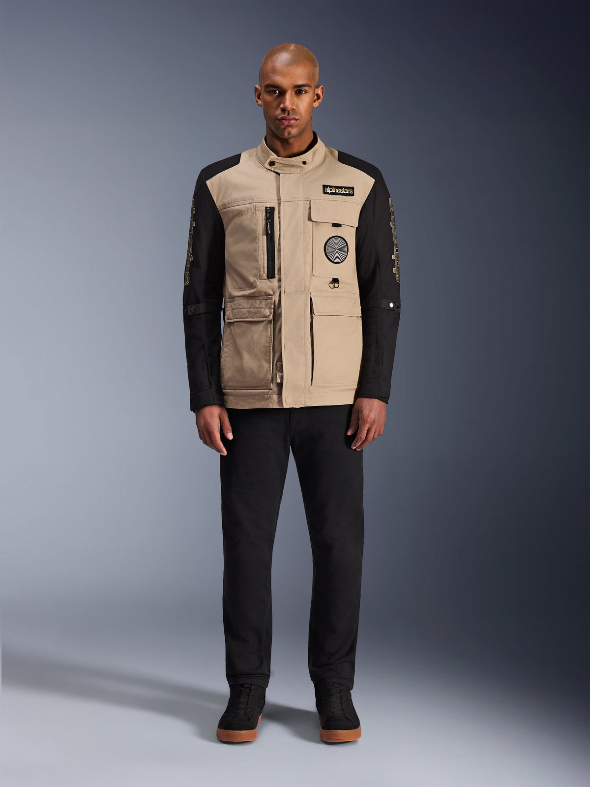 Alpinestars Dice Jacket, chaqueta de moto urbana, cuerpo color arena aluminio con mangas negras, silueta inspirada en ropa de trabajo con cuatro bolsillos frontales utilitarios, combinada con pantalones negros y zapatillas de caña alta negras, equipamiento de conducción robusto listo para la calle