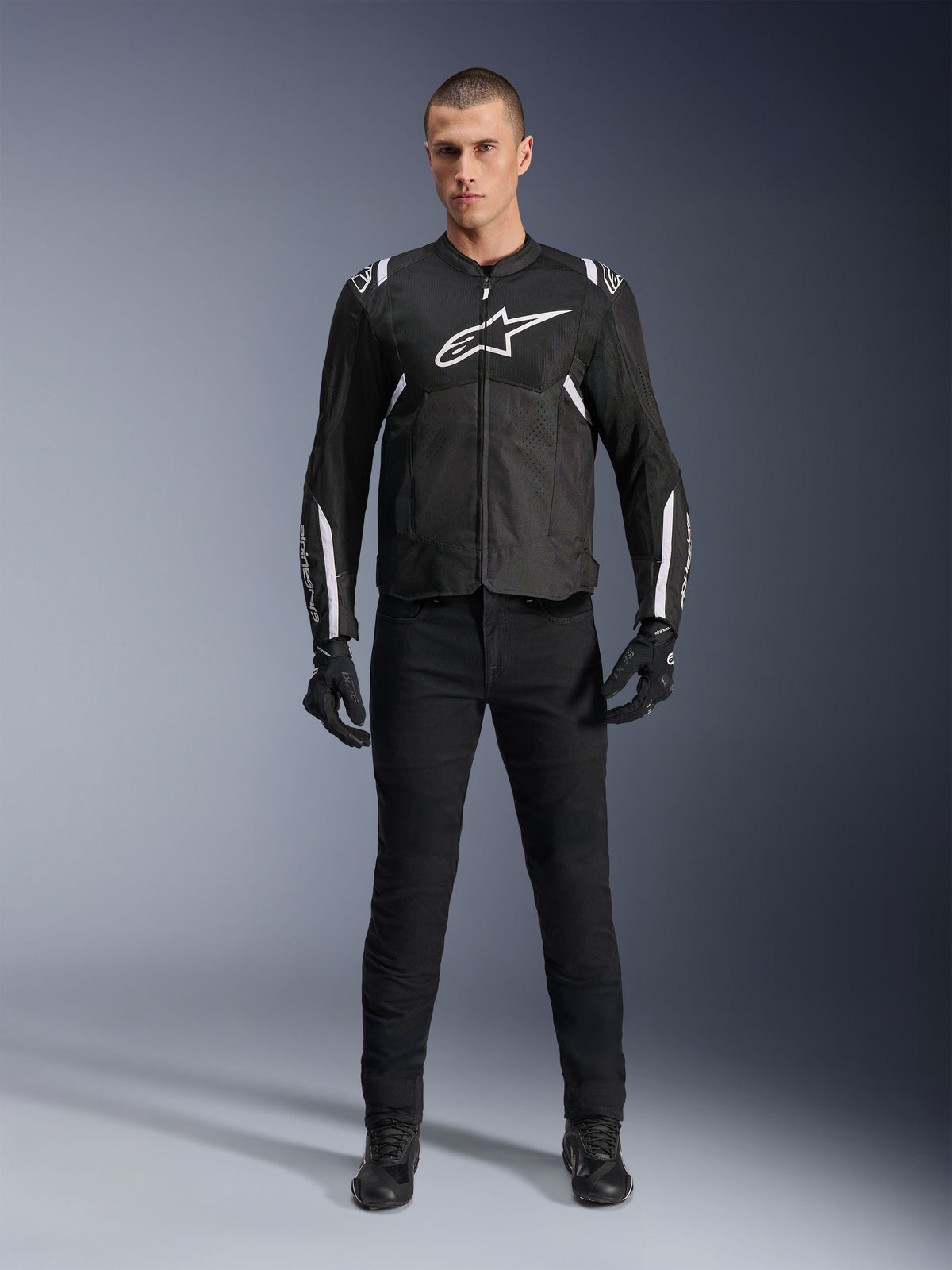 Chaqueta Alpinestars T-Sps Air V2, chaqueta de moto textil en negro y blanco, con un gran logotipo blanco en el pecho y paneles de malla, usada por un modelo con equipamiento negro para conducción deportiva urbana.
