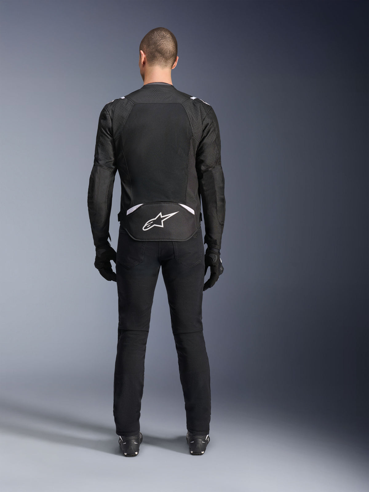 Chaqueta Alpinestars T-Sps Air V2, vista trasera, chaqueta de moto textil en negro y blanco, con un gran panel de malla en la espalda para un flujo de aire máximo y logotipo de Astars en blanco en la parte inferior de la espalda, combinada con pantalones y guantes de conducción negros