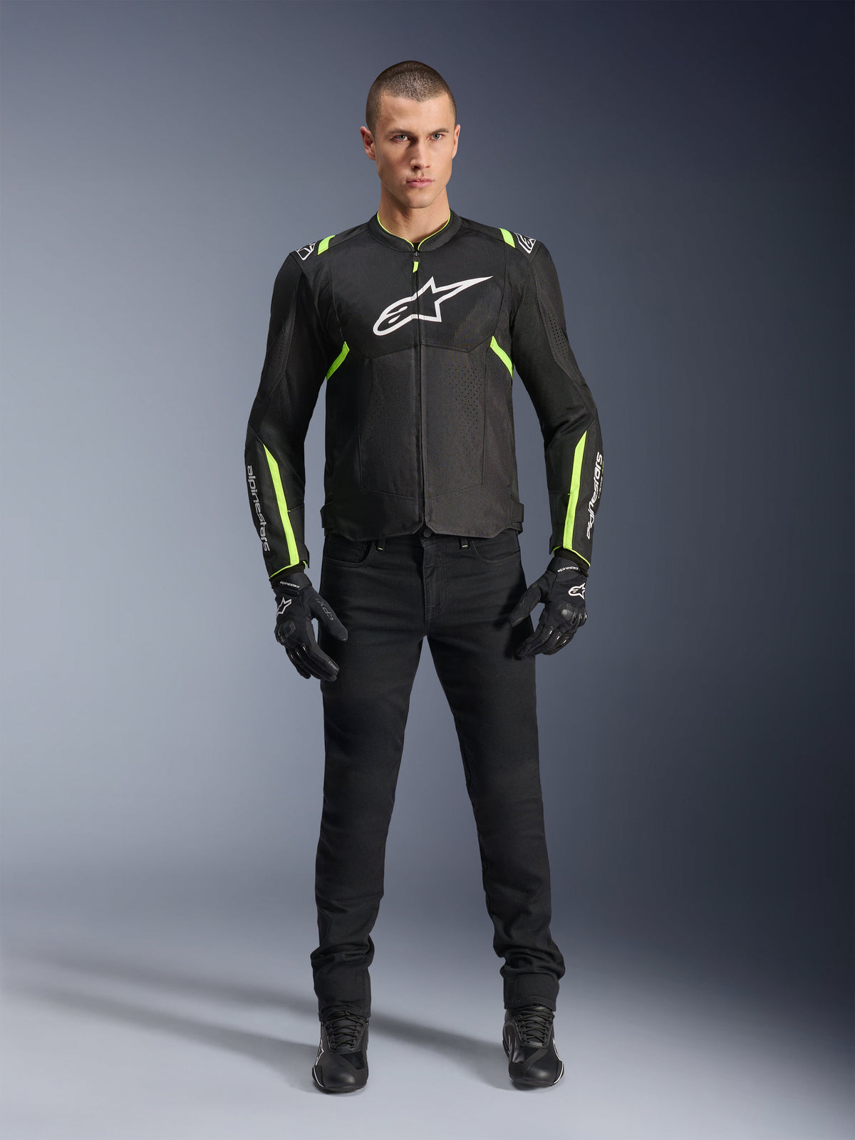 Chaqueta Alpinestars T-Sps Air V2, negro y amarillo flúor, chaqueta textil de moto con paneles de malla, usada por un modelo masculino con pantalones y guantes negros, con el logotipo blanco de Alpinestars en el pecho, equipamiento de conducción deportiva urbana