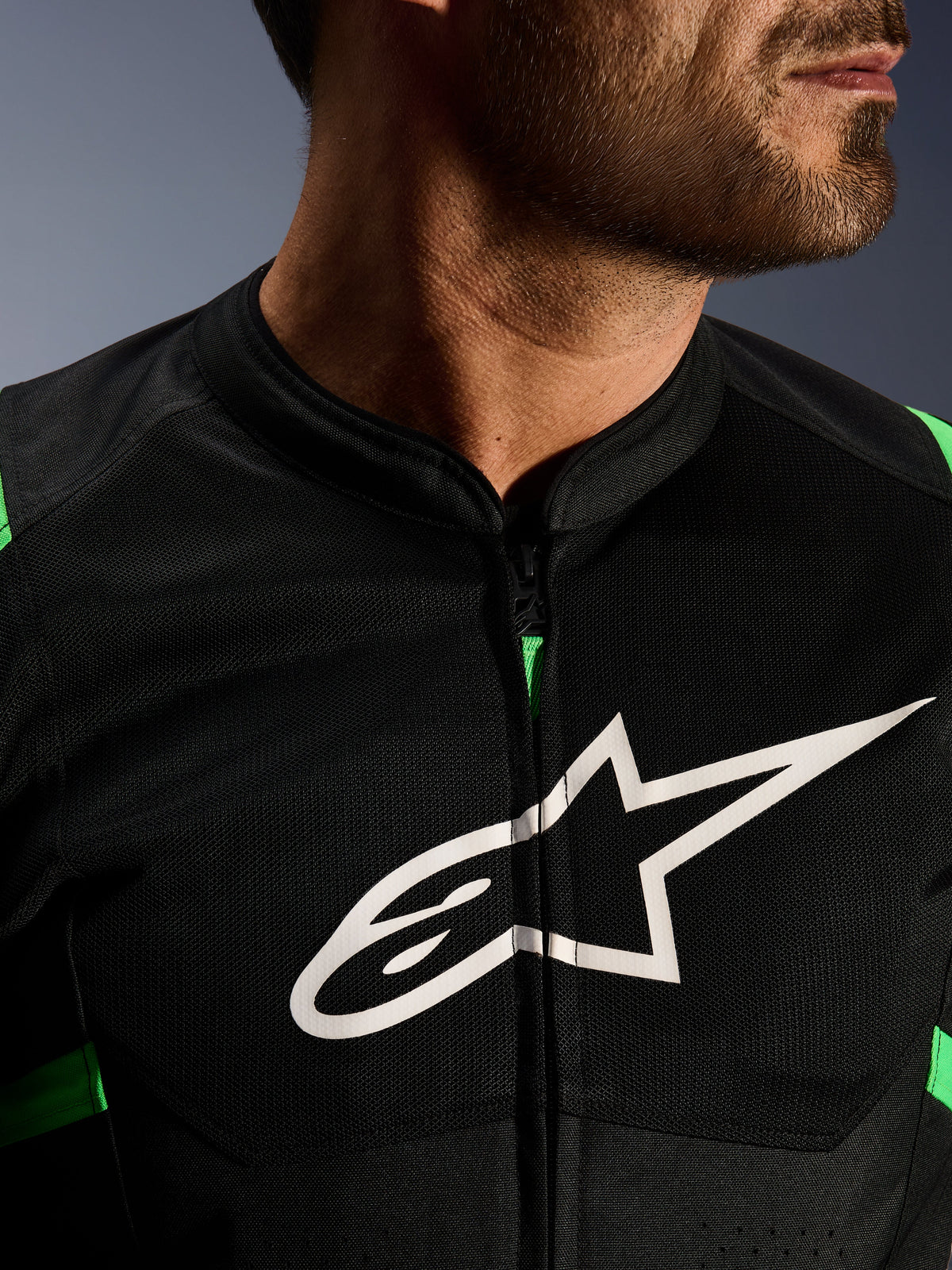 Primer plano de la chaqueta Alpinestars T-SPS Air V2, en color negro y verde flúor, con paneles de malla técnica transpirable, cremallera central y el destacado logotipo blanco de la estrella de Alpinestars en el pecho, equipamiento de motociclismo de alto rendimiento