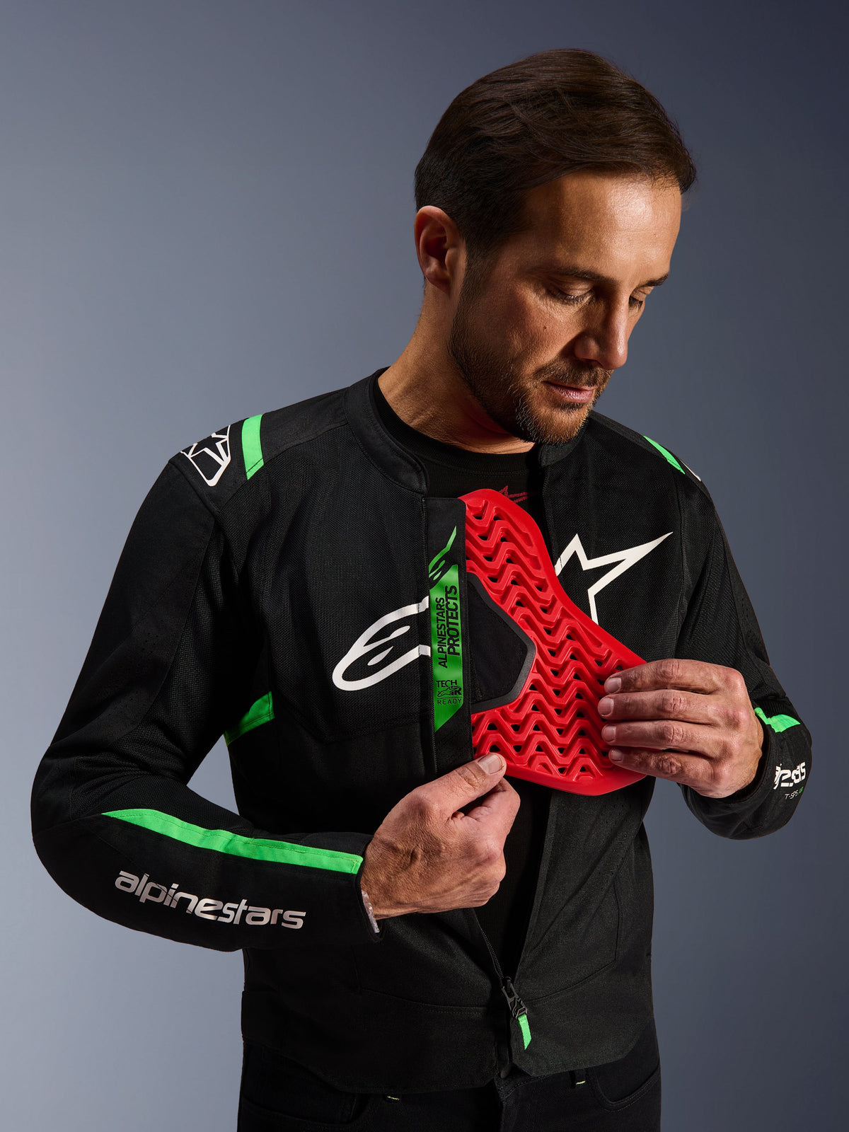 Chaqueta Alpinestars T-SPS Air V2, chaqueta de moto en negro y verde flúor, hombre mostrando el inserto de protector de pecho Nucleon en color rojo, etiqueta Tech-Air® Ready, diseño textil deportivo con paneles de malla