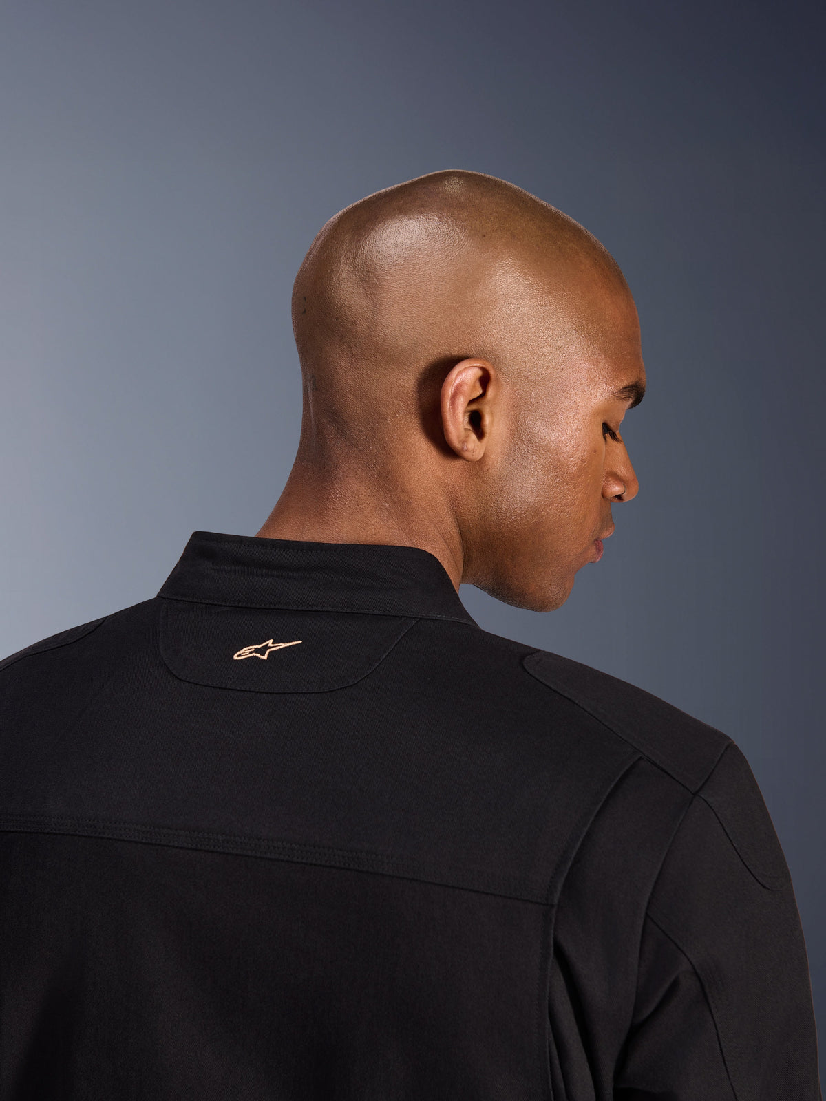 Chaqueta Alpinestars Bruiser, negra, detalle posterior del cuello y los hombros, con un pequeño logotipo de Alpinestars bordado en color canela, chaqueta de moto urbana con estética de ropa de trabajo