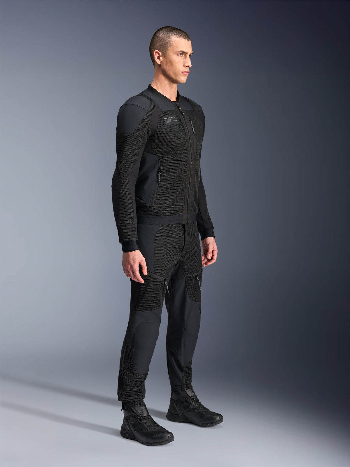 Chaqueta Alpinestars Troop-Air Pro, chaqueta técnica de aire blindada, color negro, usada por un modelo con pantalones y botas de moto negros a juego, con una estructura avanzada de malla técnica 2D y paneles de ventilación transpirables, equipamiento de conducción urbano contemporáneo.