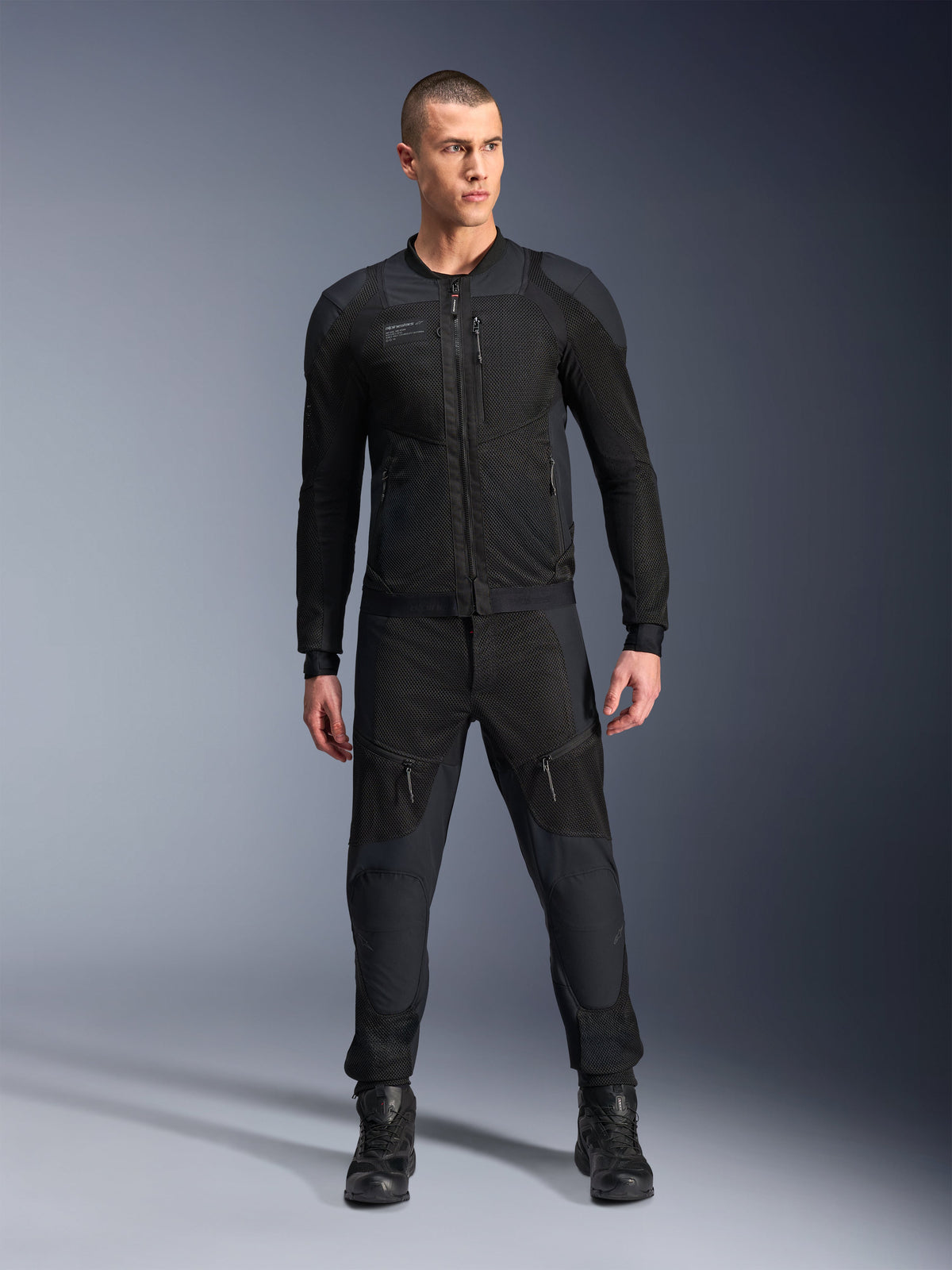 Chaqueta Alpinestars Troop-Air Pro, chaqueta de moto técnica blindada en color negro, con paneles de malla y cremalleras frontales, combinada con pantalones negros a juego y botas de moto, equipamiento urbano premium para carretera