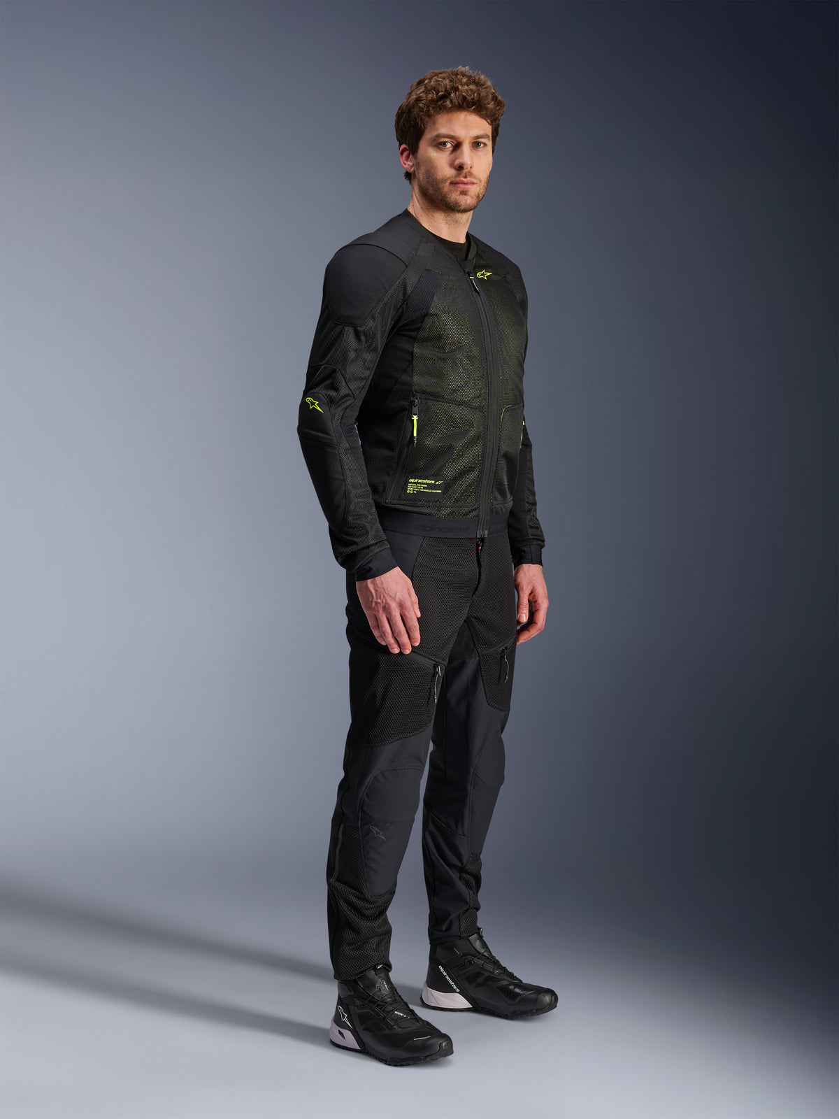 Chaqueta Alpinestars Troop-Air, chaqueta de malla para moto, negro y amarillo flúor, usada por un modelo con pantalones negros y calzado de conducción a juego, cuenta con una construcción de malla de alto flujo de aire con detalles amarillos fluorescentes en el pecho y las mangas, diseño técnico ligero para conducción en carretera