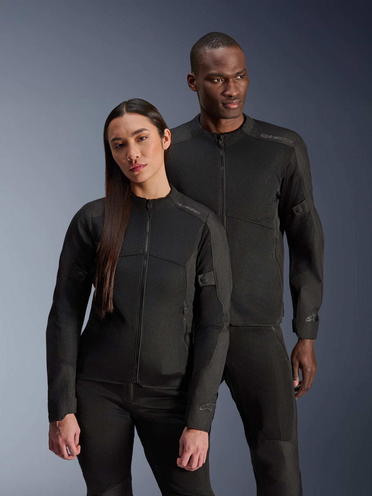 Chaqueta Alpinestars Stella C-1 Air, negra, lucida por un modelo masculino y una modelo femenina, construcción de malla técnica para el flujo de aire, logotipos reflectantes, equipamiento urbano elegante para motociclistas