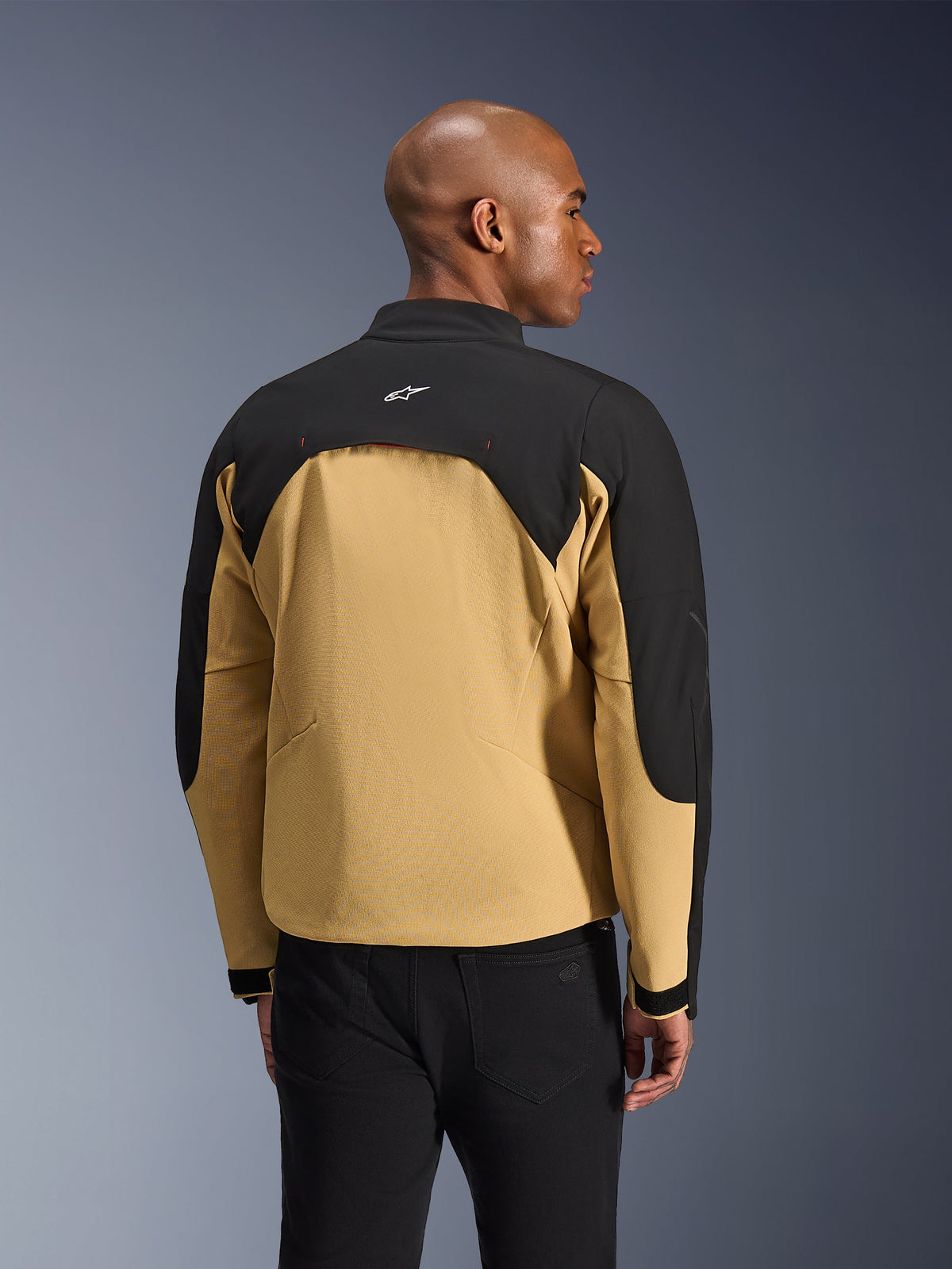 Chaqueta Alpinestars Provoke, chaqueta urbana para motocicleta, negro y camel, vista trasera que muestra la construcción bicolor, panel de ventilación posterior con forro de malla, pequeño logotipo blanco en la parte superior de la espalda, combinada con pantalones negros