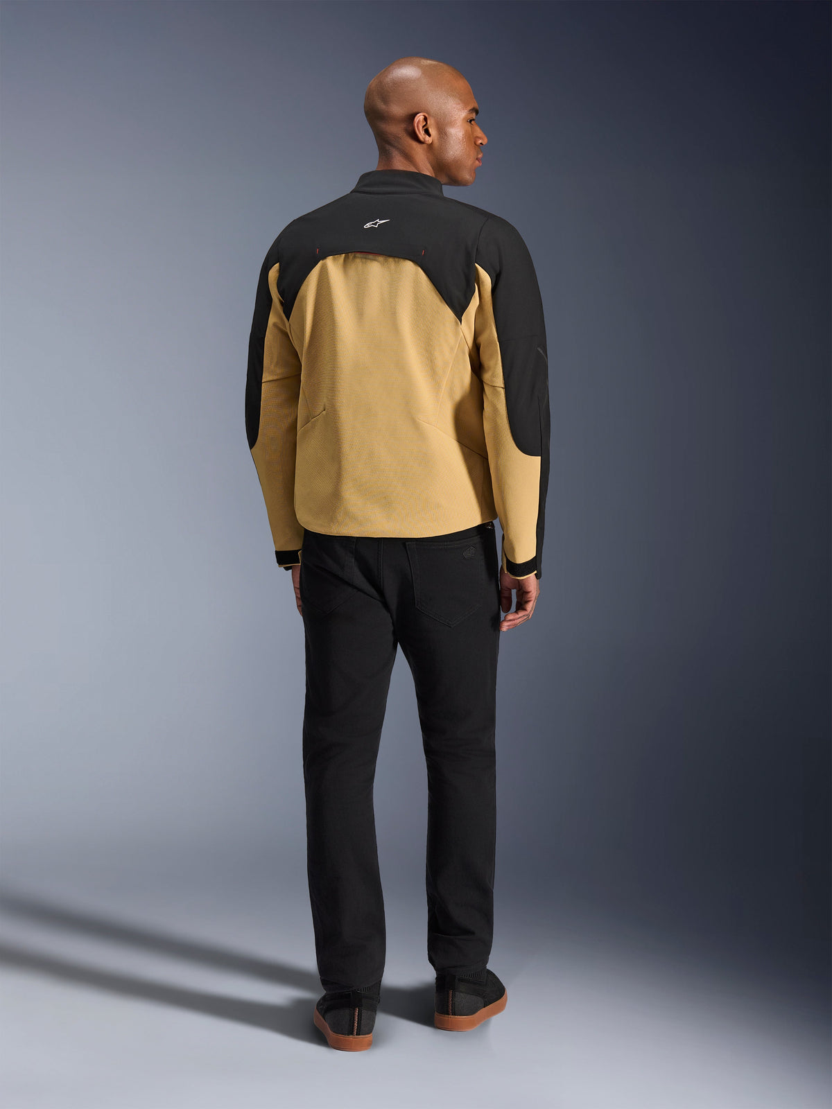 Chaqueta Alpinestars Provoke, Negro y Camel, vista trasera de chaqueta de moto urbana con canesú superior negro y parte inferior de la espalda en camel, usada por un modelo con pantalones negros, diseño contemporáneo inspirado en el streetwear